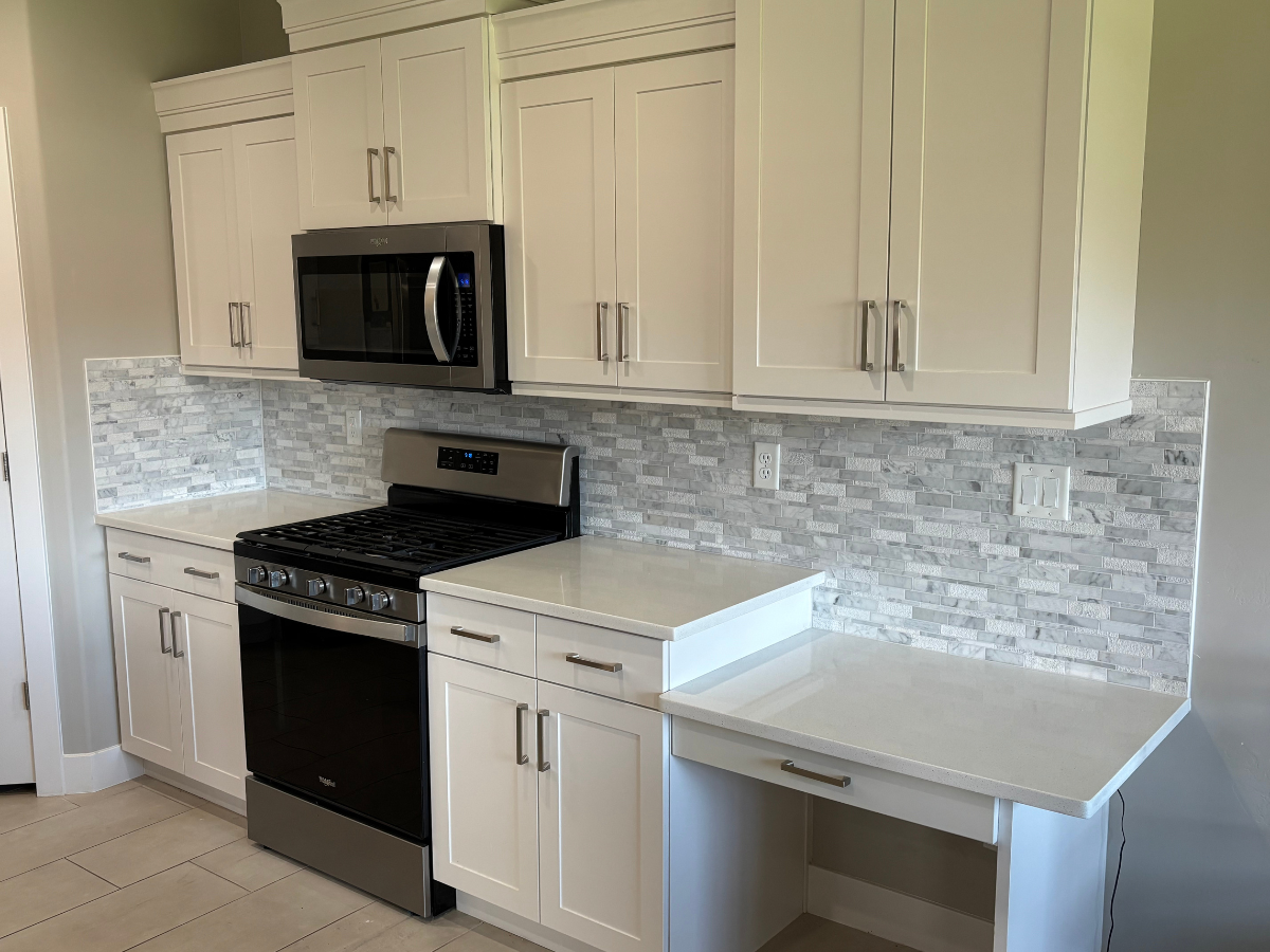 A kitchen featuring white cabinets, a stainless steel stove and microwave, a white countertop, and a marble-tiled backsplash.