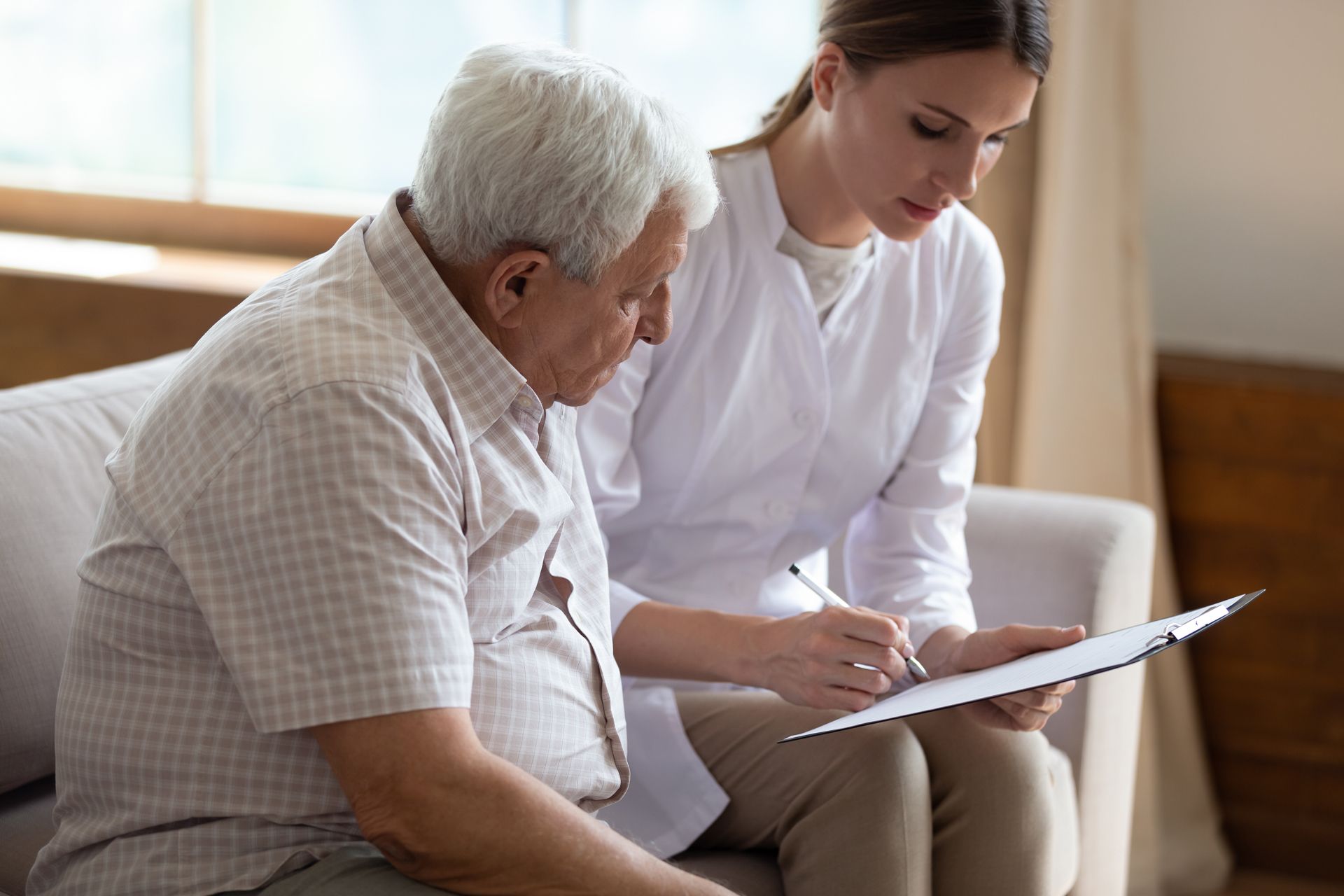 Woman in white coat pointing to document for seated older person.