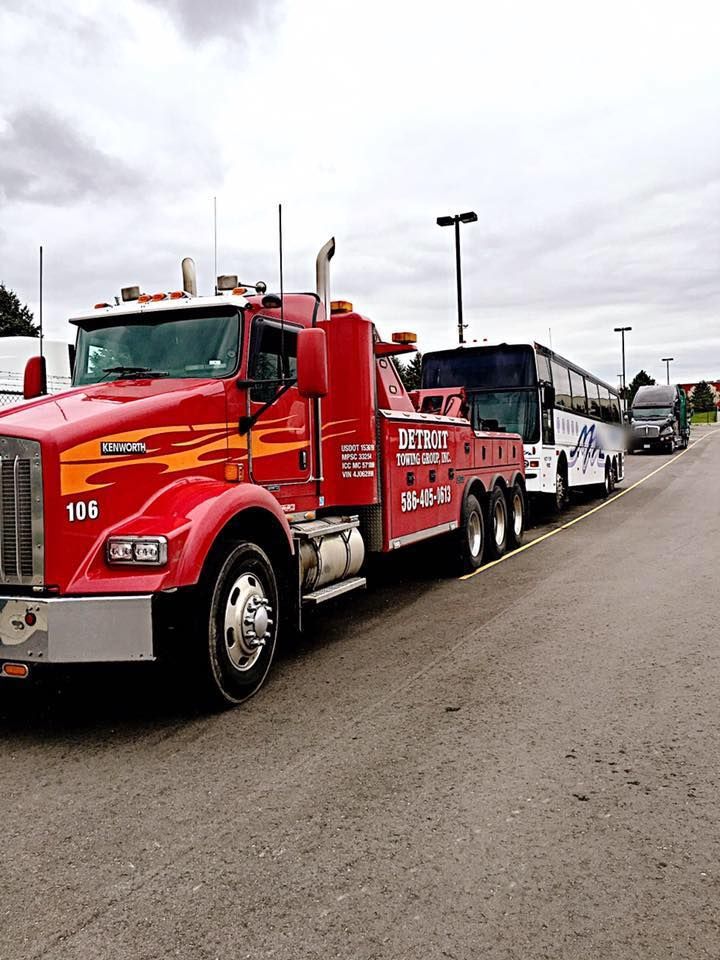 Red tow truck towing a bus on a paved road under a cloudy sky.