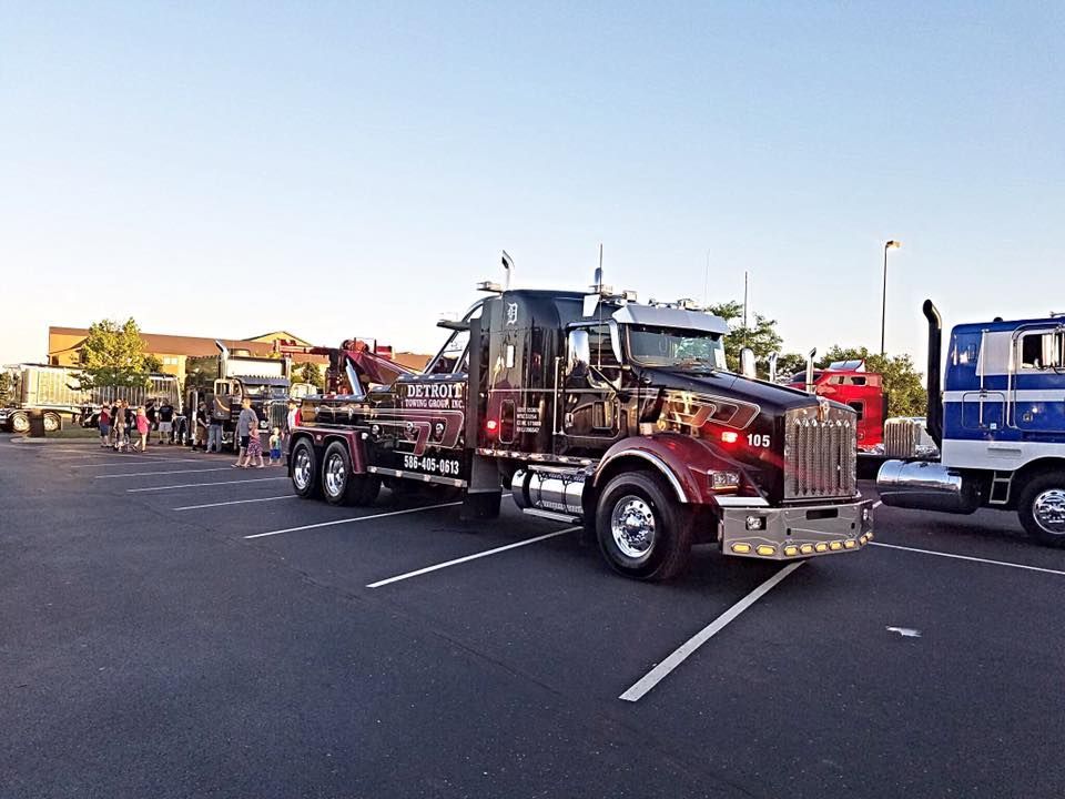 A large maroon tow truck parked in a lot, with people in the background.