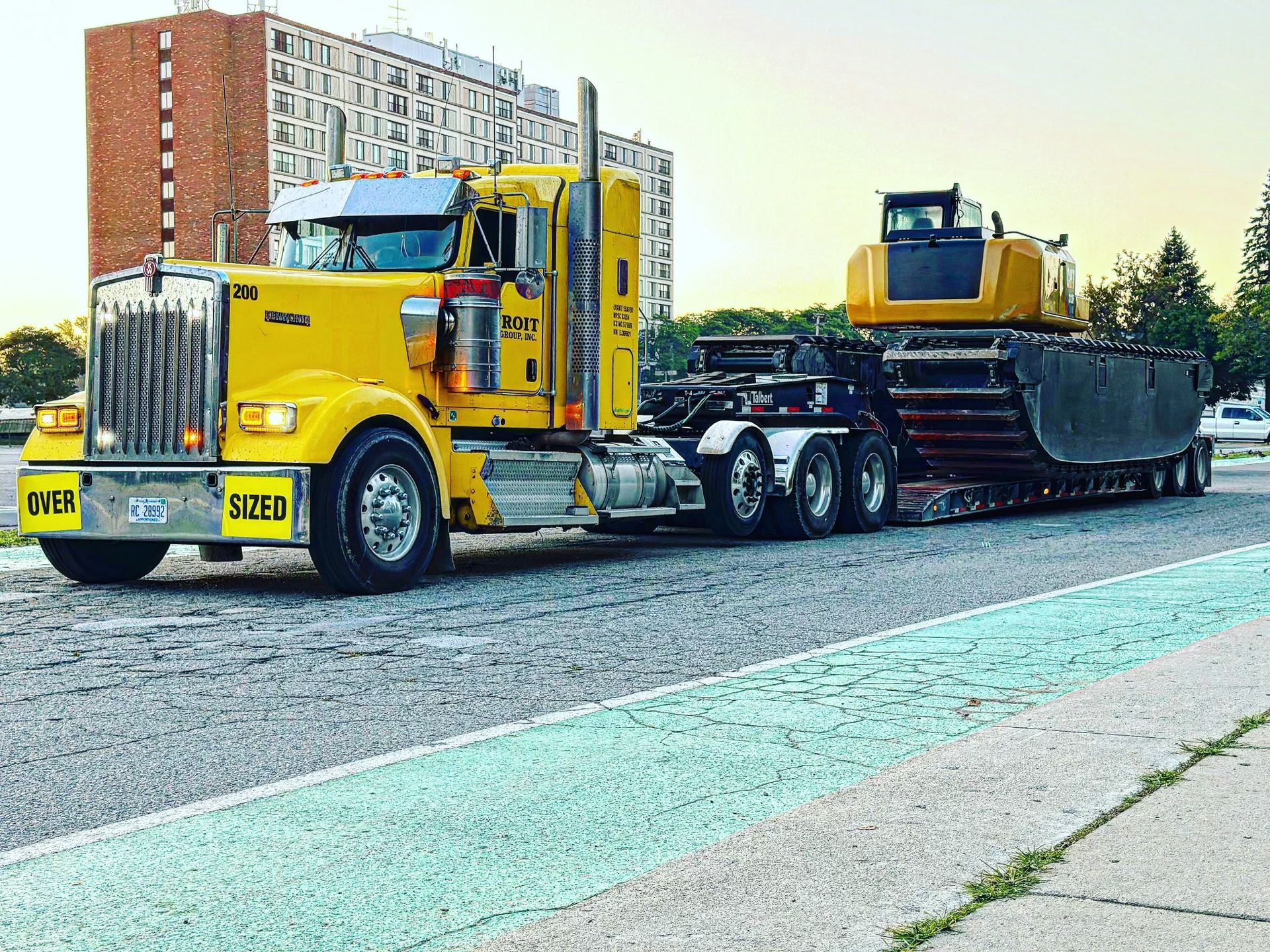 Yellow semi-truck transporting a large excavator on a lowboy trailer; parked on pavement.