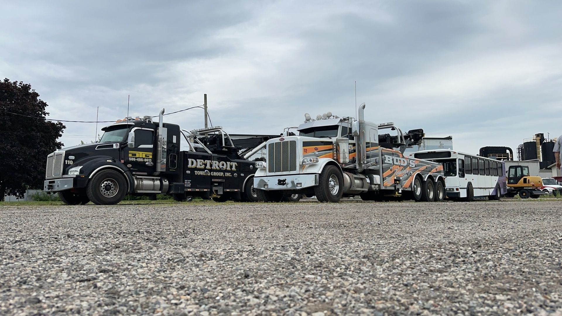 A row of tow trucks parked on gravel under a cloudy sky.