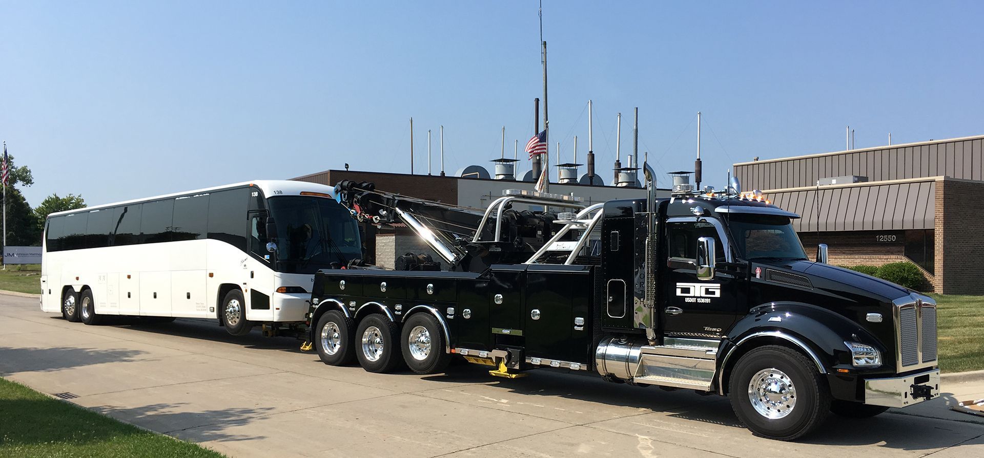 Black tow truck towing a white bus on a sunny day.