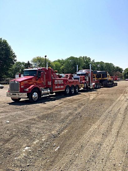 Red tow truck towing a semi-truck on a gravel lot under a clear sky.