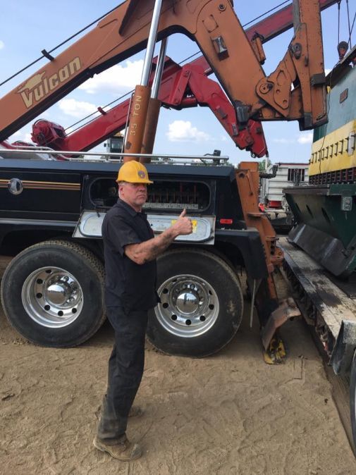 Man in hard hat giving thumbs up next to a tow truck with an orange boom.