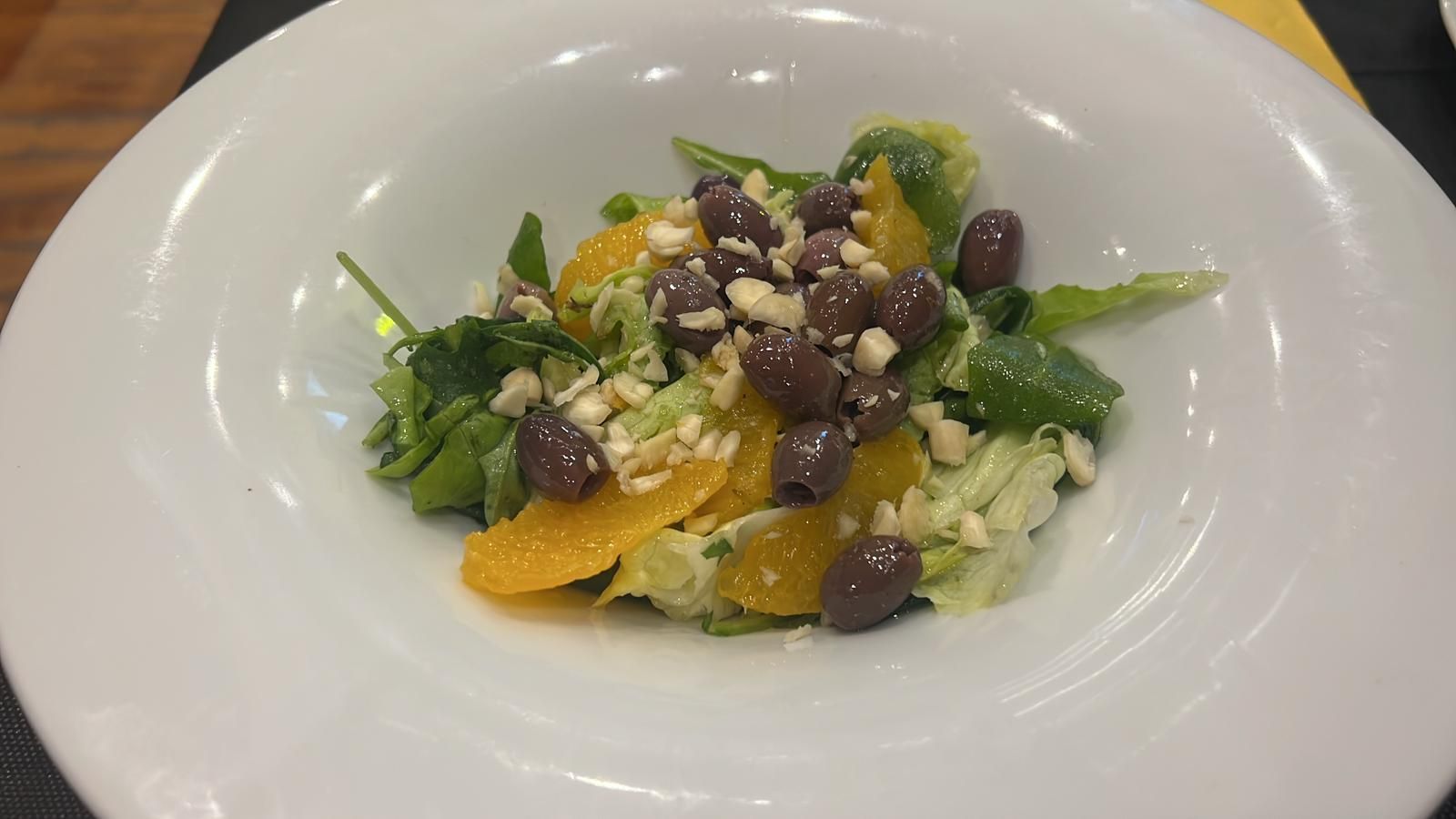 Insalata con olive, fette d'arancia, noci e verdure in una ciotola bianca.