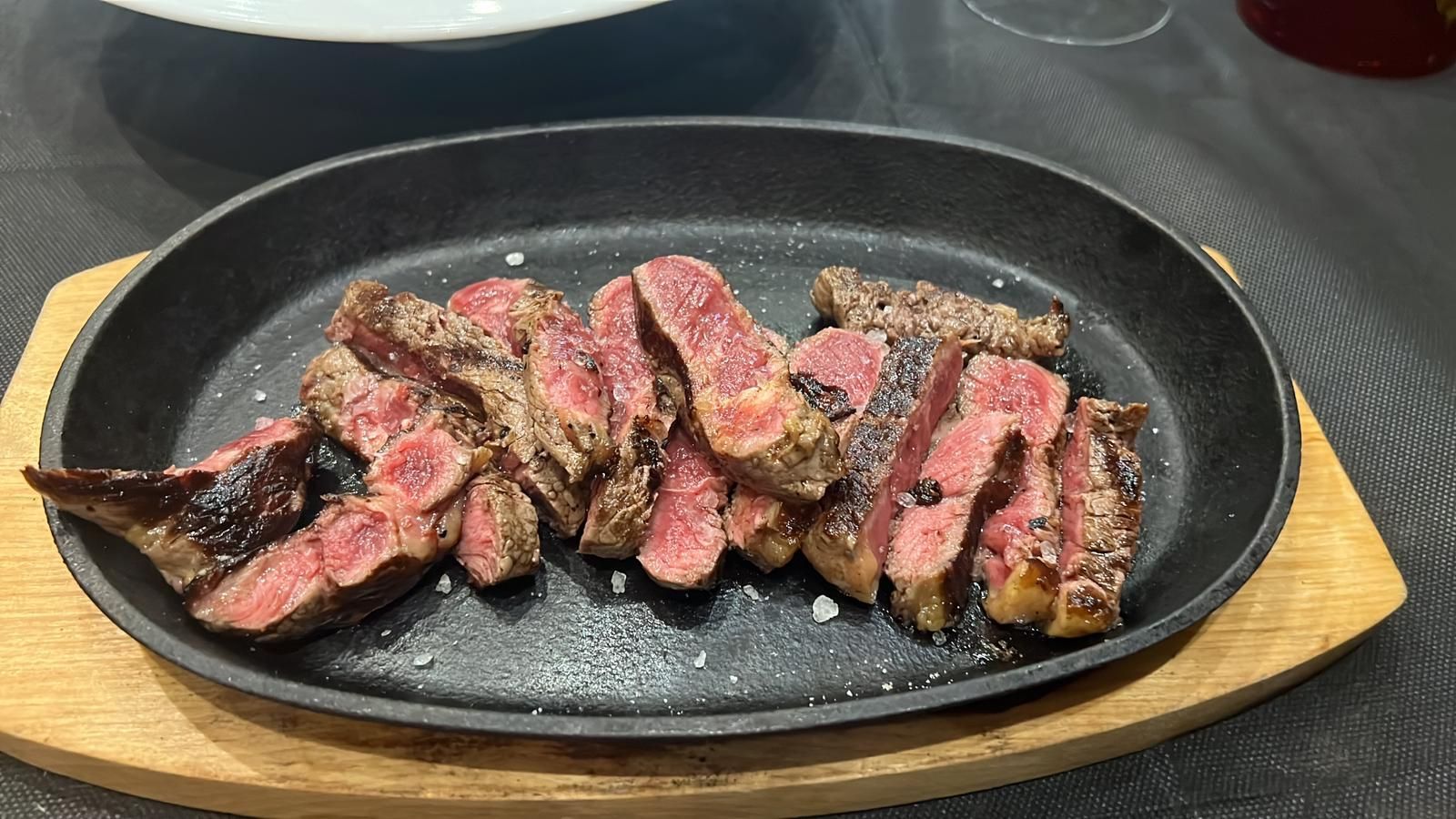 Bistecca tagliata a fette su una piastra di ghisa calda, guarnita con sale.