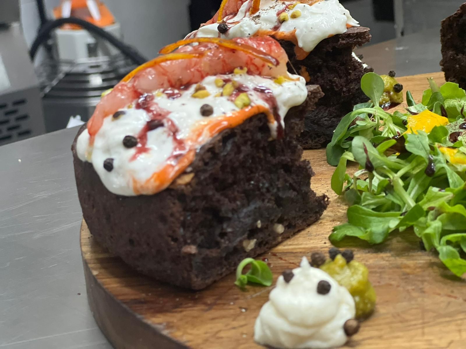 Dessert al cioccolato con gamberi e panna, servito su un tagliere di legno accanto a un'insalata verde.