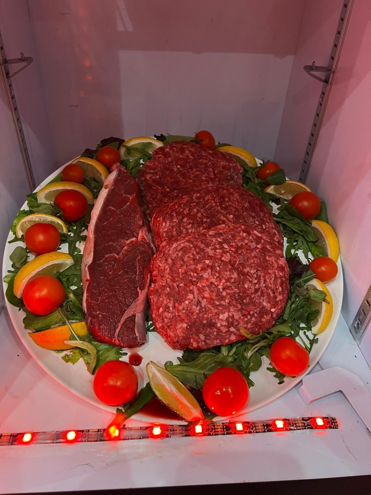Bistecche crude, carne macinata, pomodori e fette di limone su un piatto decorato.