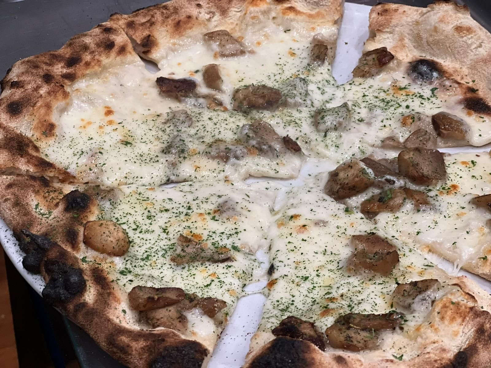 Pizza bianca con funghi e salsiccia, tagliata a fette e cosparsa di erbe aromatiche.