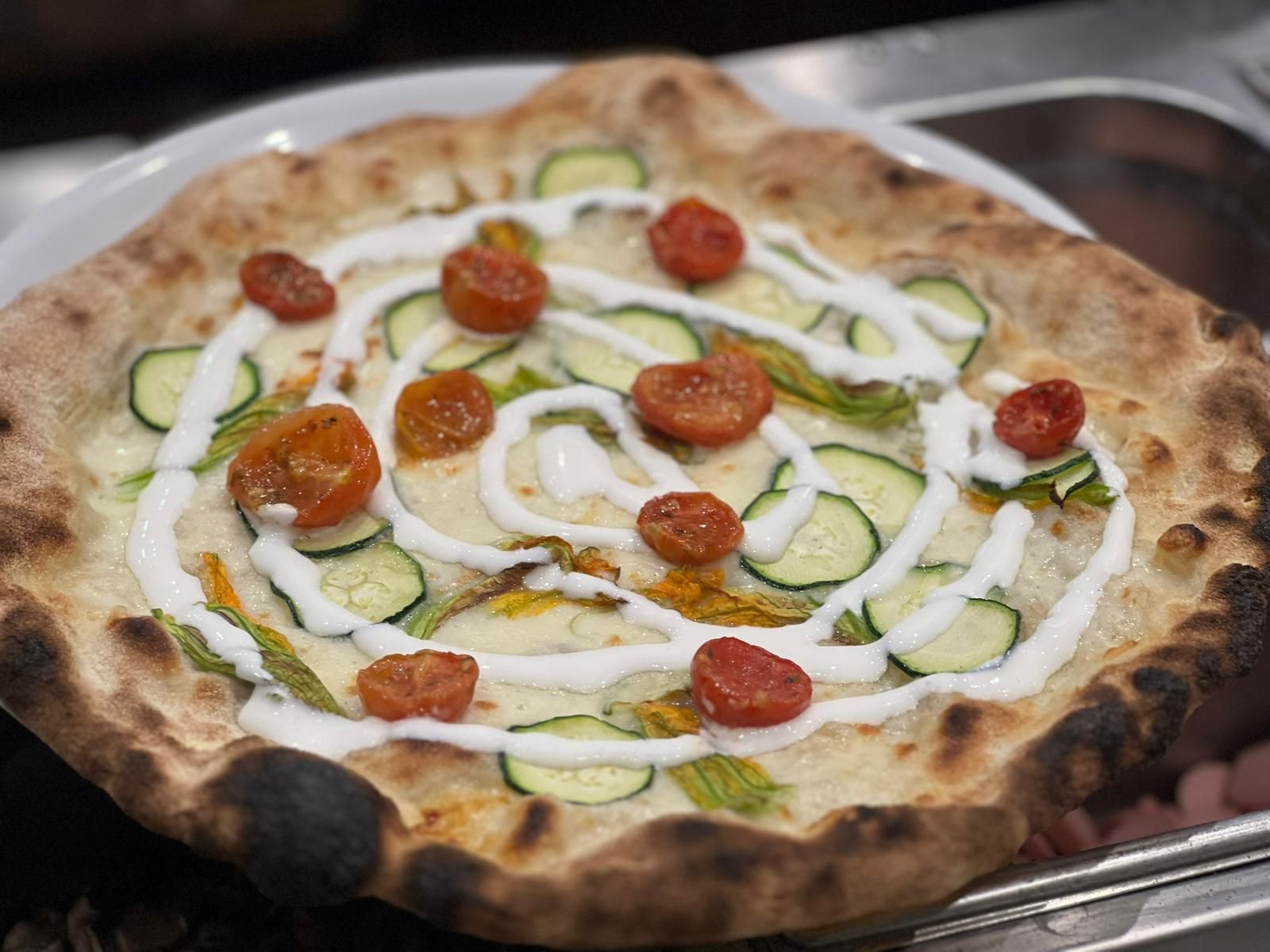 Pizza condita con zucchine, pomodori e salsa cremosa.