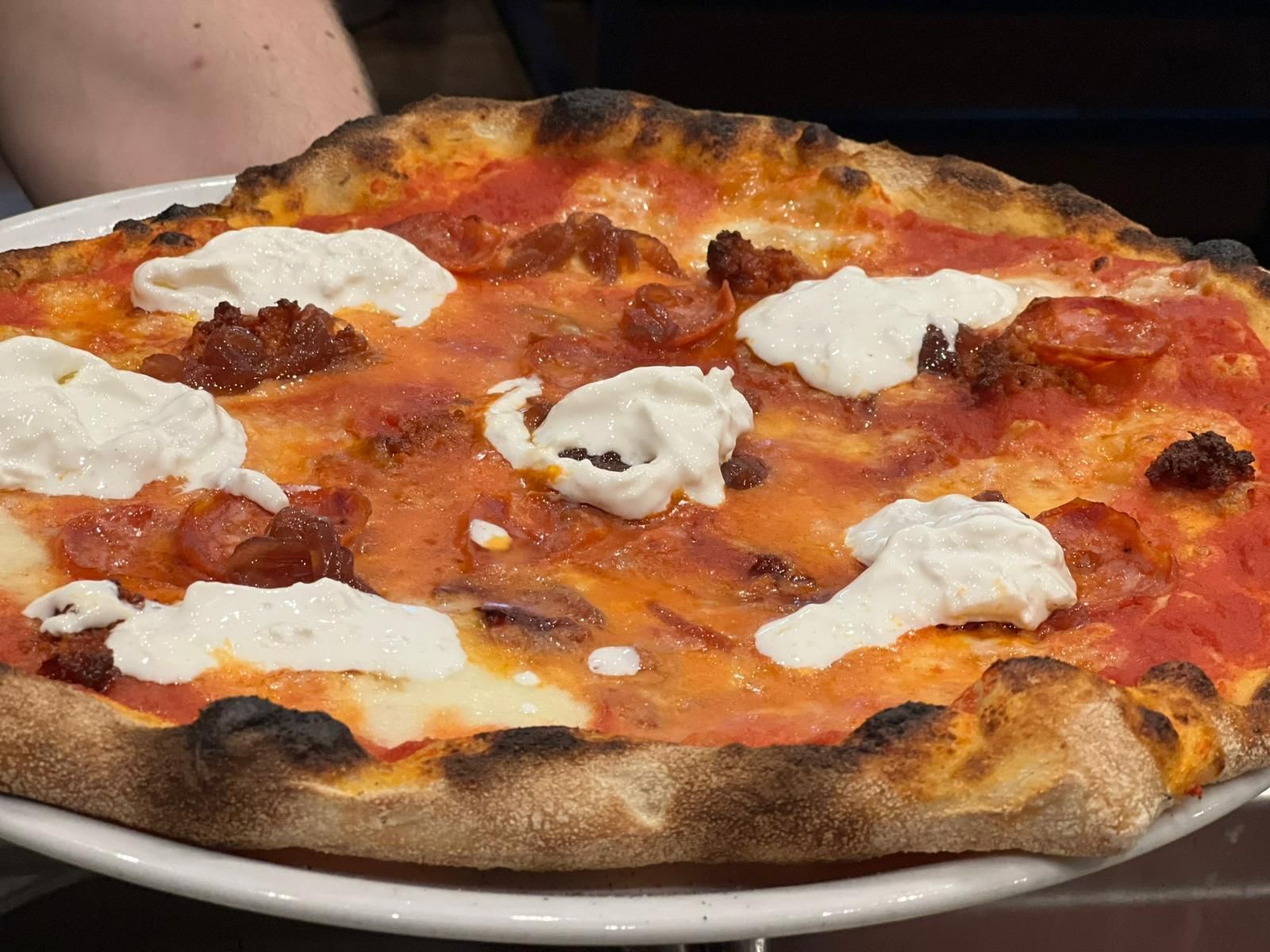 Pizza su un piatto bianco: salsa di pomodoro, chorizo e cucchiaiate di ricotta bianca, la crosta è bruciacchiata.