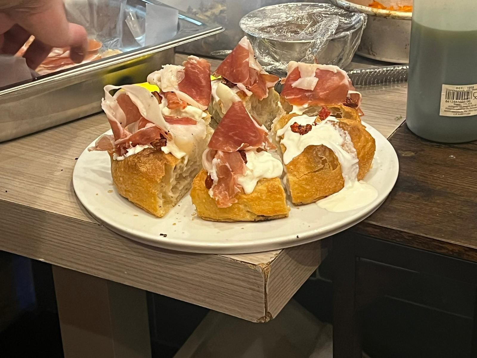Piatto di fette di baguette condite con prosciutto, panna e altri ingredienti, disposto su una superficie di legno.