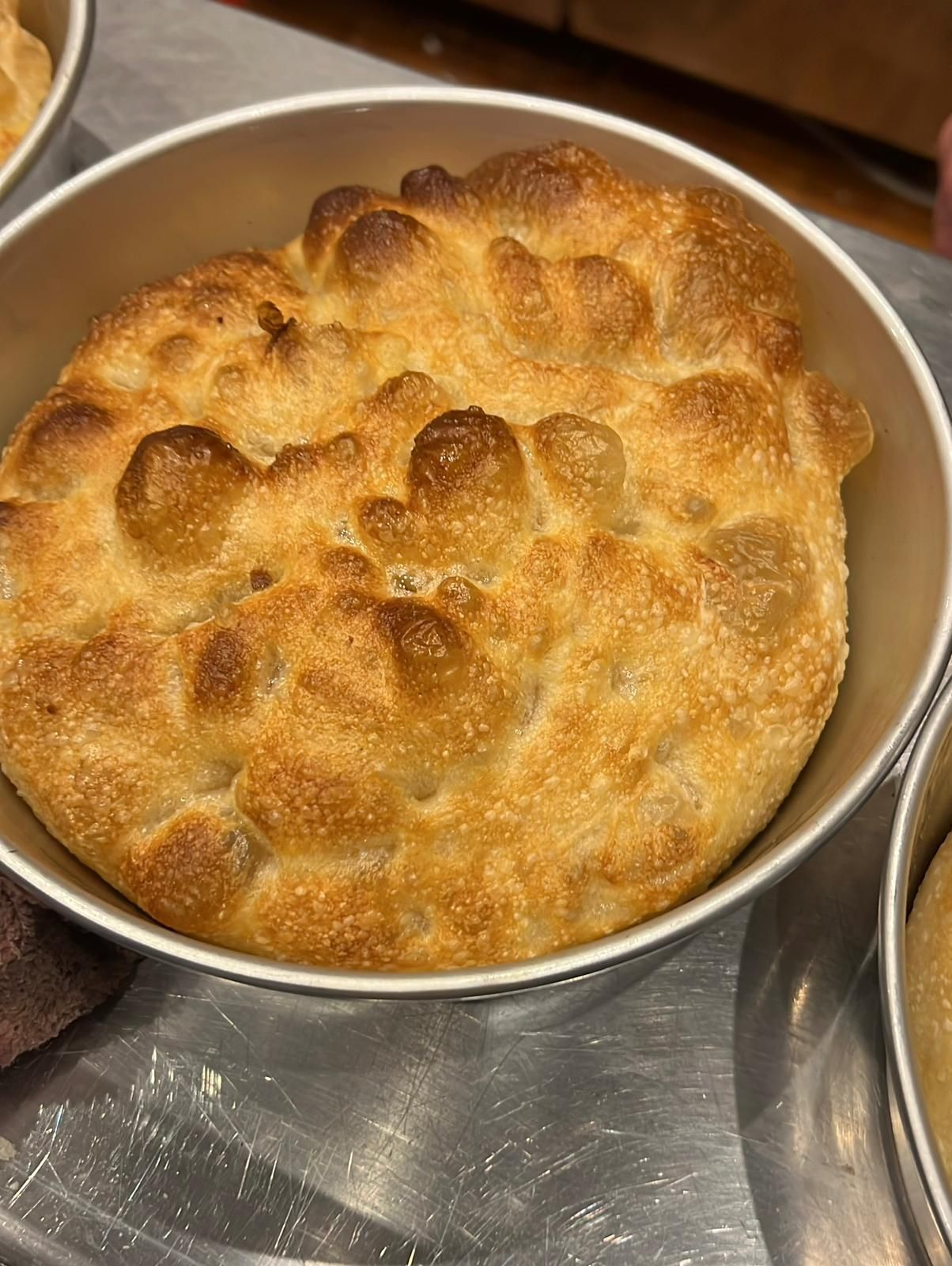 Focaccia dorata in una teglia rotonda di metallo, croccante e con bolle d'aria.