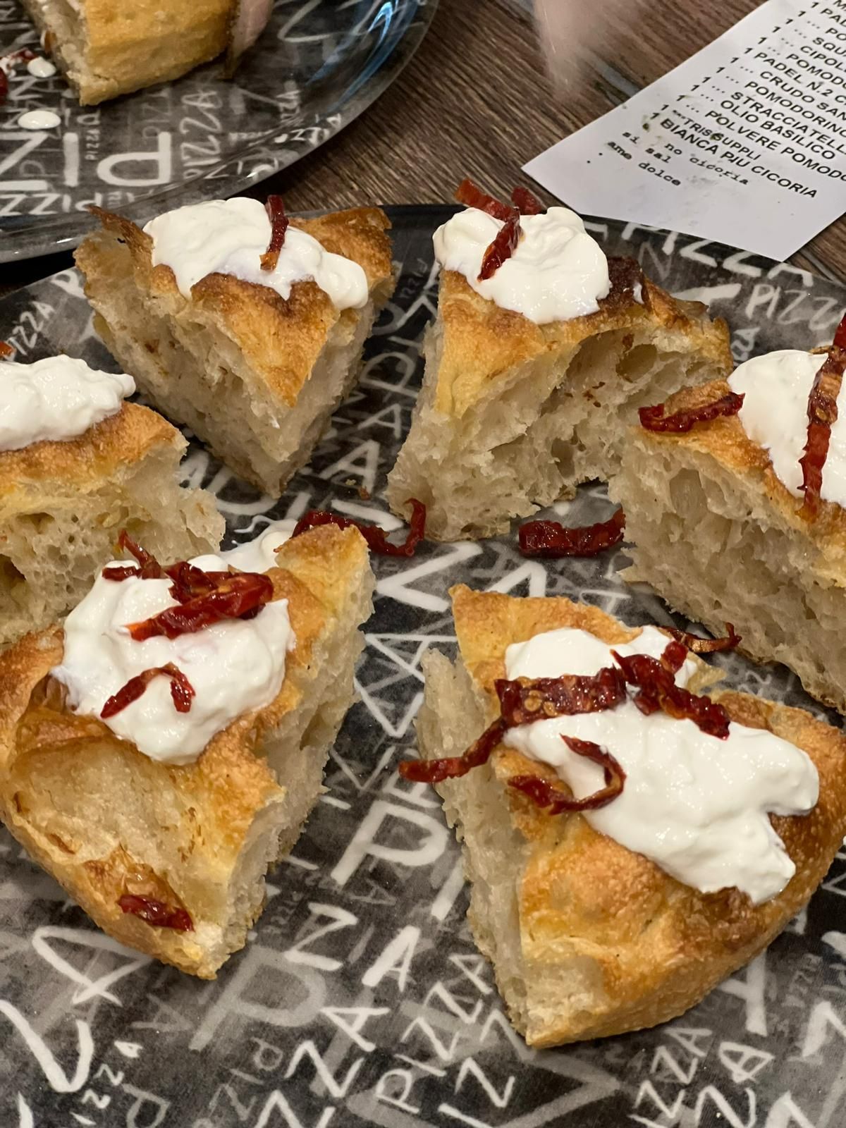 Fette di focaccia condite con formaggio bianco e pomodori secchi su un piatto decorato.