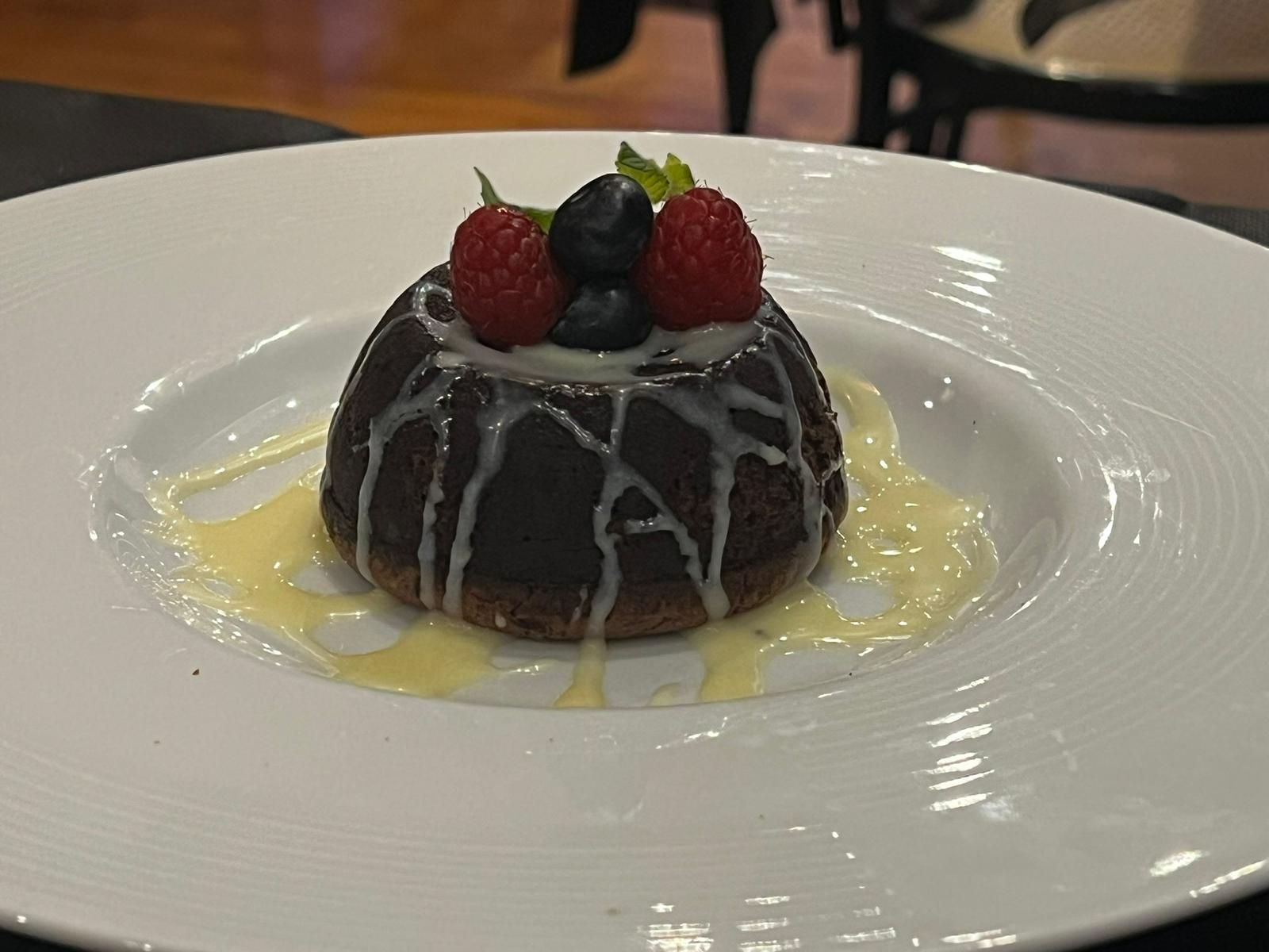 Torta al cioccolato con glassa bianca, frutti di bosco e salsa, su un piatto bianco.
