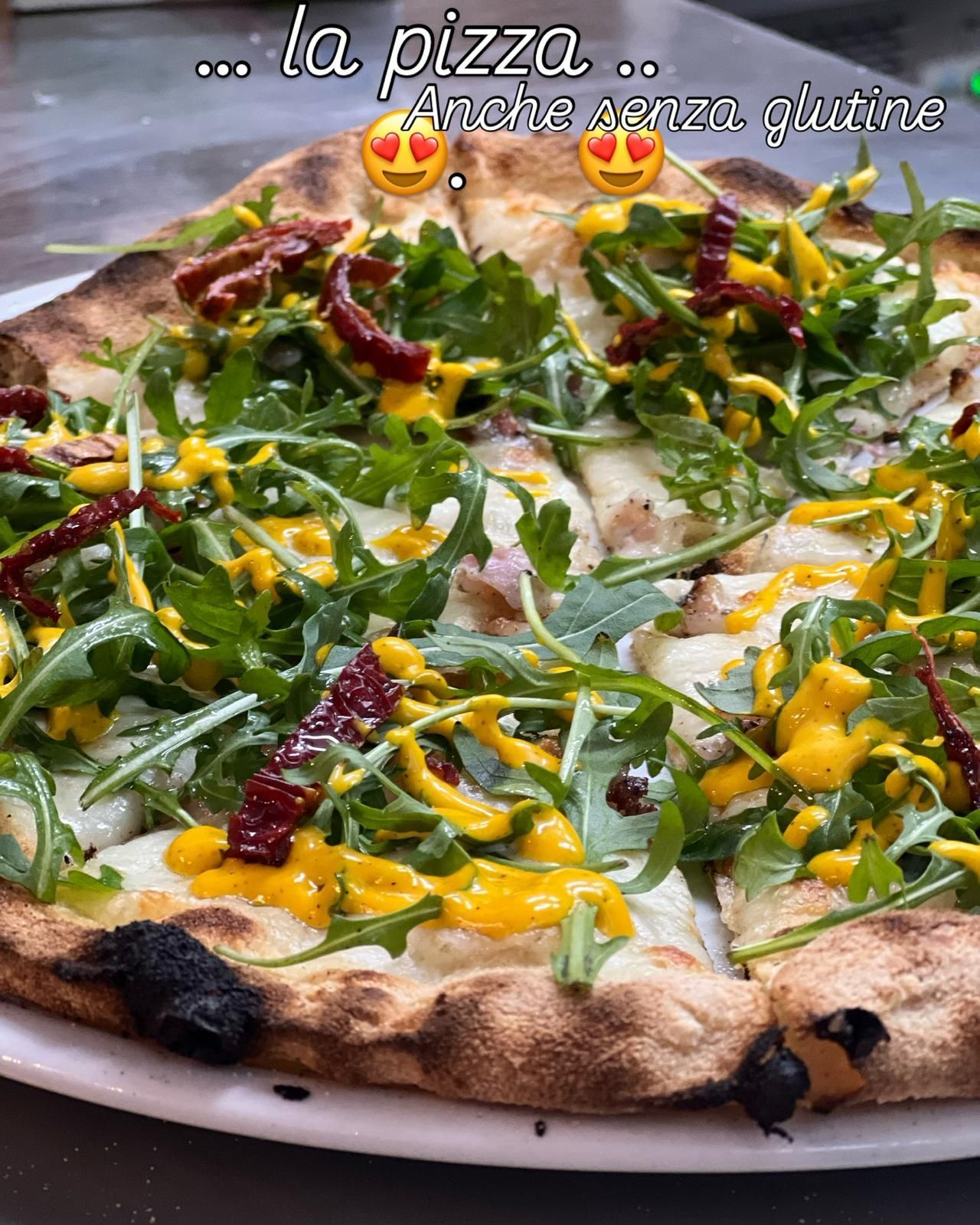 Pizza senza glutine condita con rucola, pomodori secchi e salsa gialla.