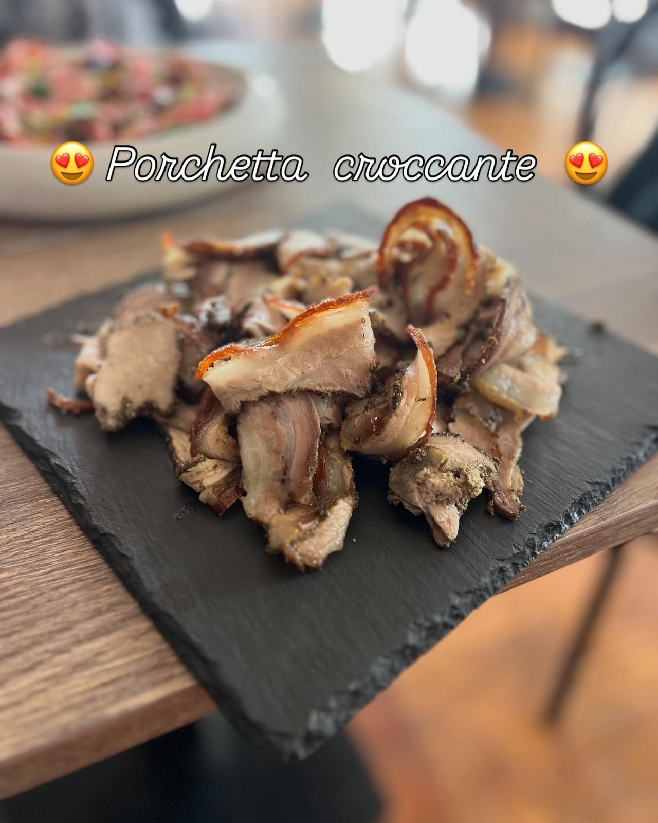 Primo piano di porchetta croccante tagliata a fette, servita su una lavagna nera.
