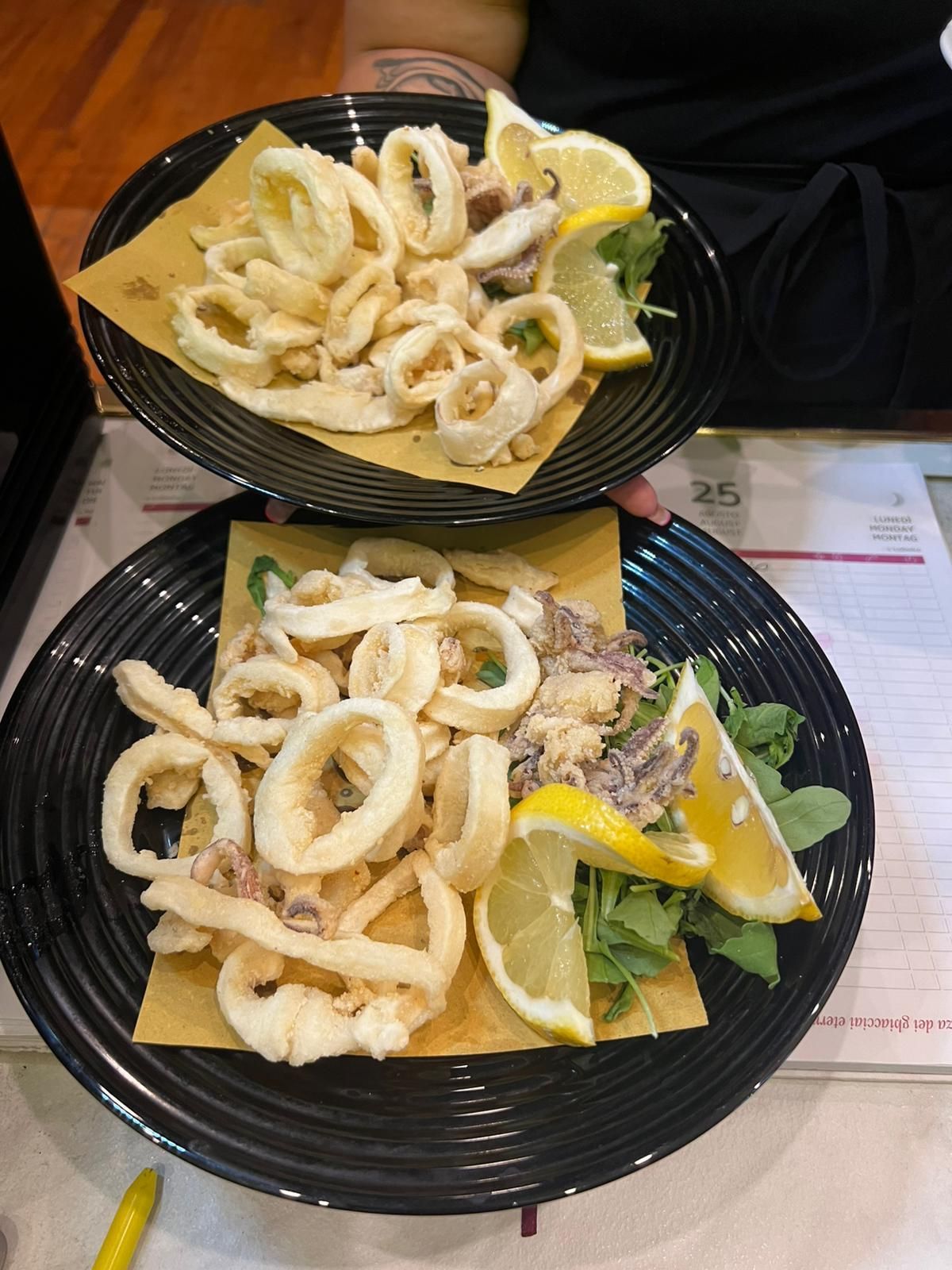 Due piatti di calamari fritti con spicchi di limone e verdure su un tavolo.