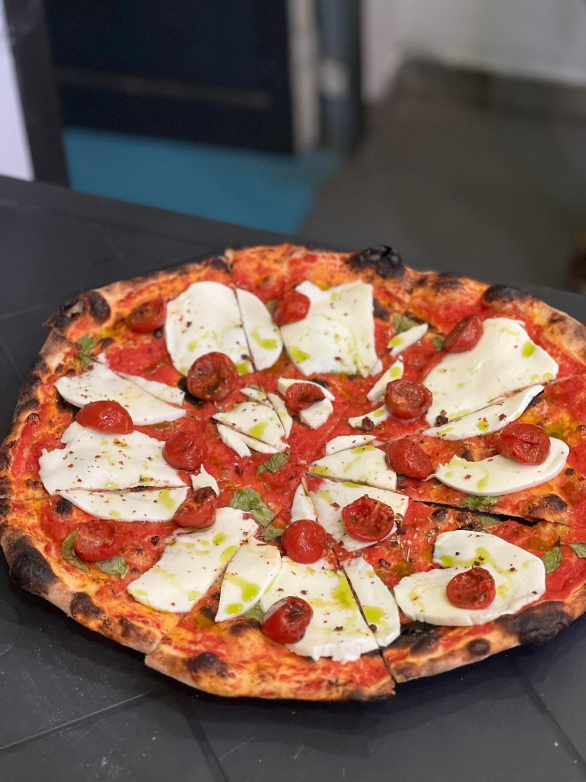 Pizza con salsa di pomodoro, mozzarella e pomodorini su un tavolo nero.