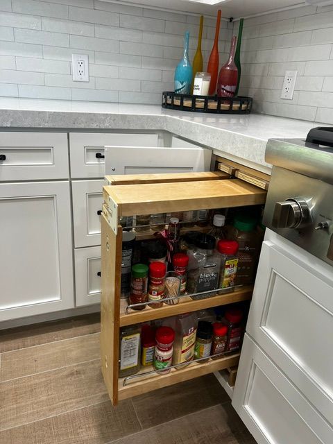 A kitchen with white cabinets and a pull out spice rack.