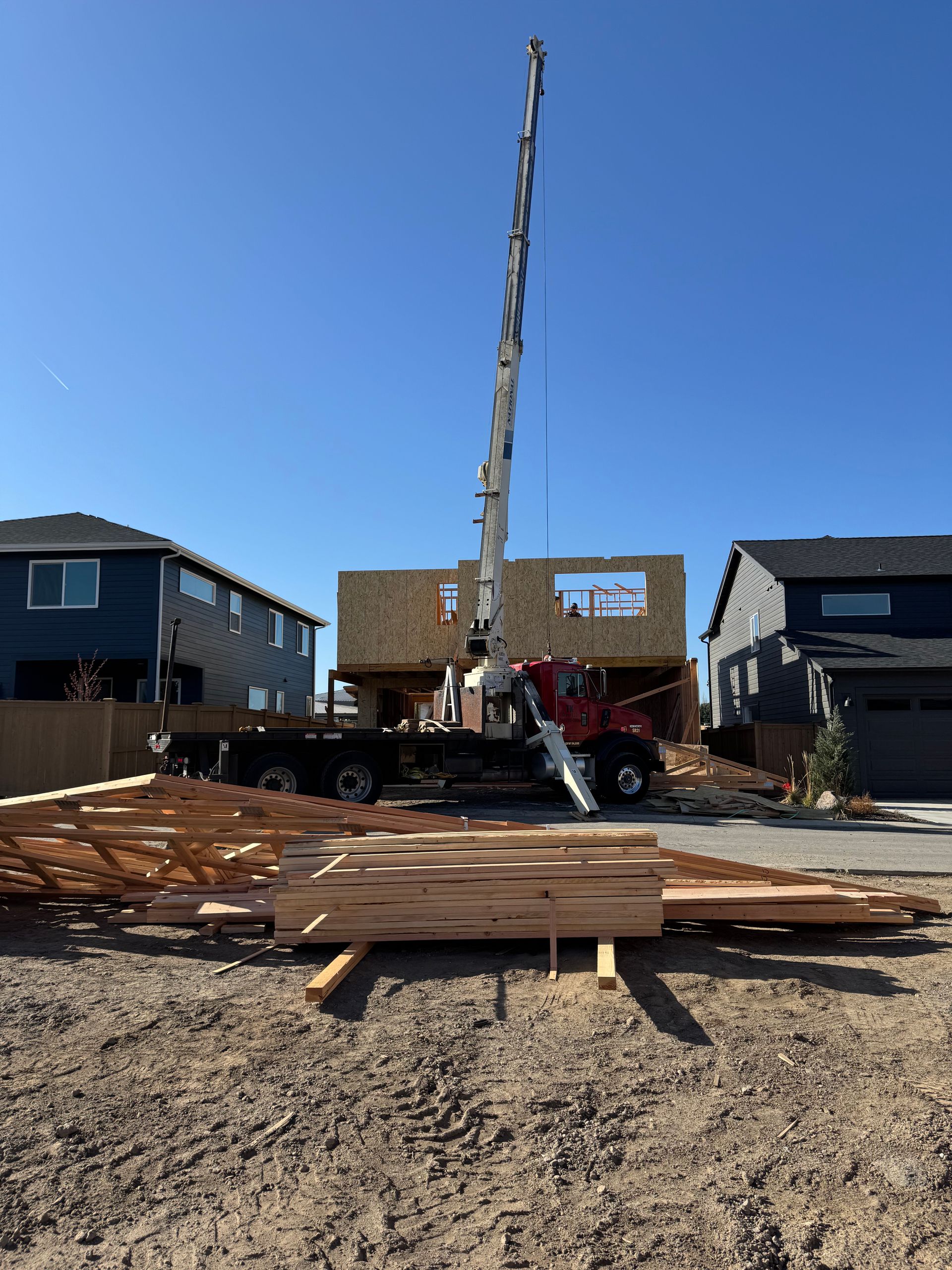 A crane is lifting a piece of wood in front of a house under construction.