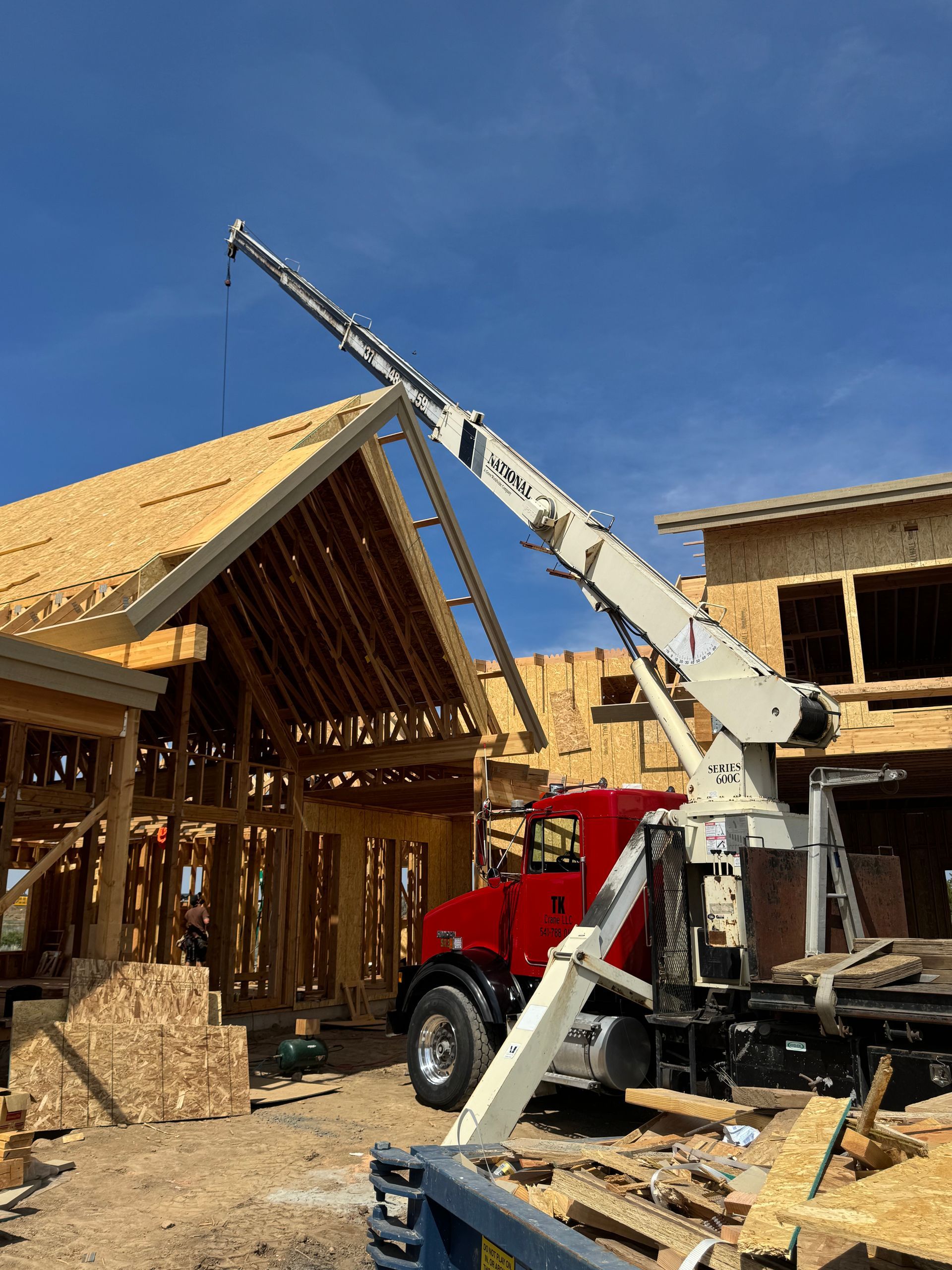 A red truck with a crane attached to it is parked in front of a house under construction.