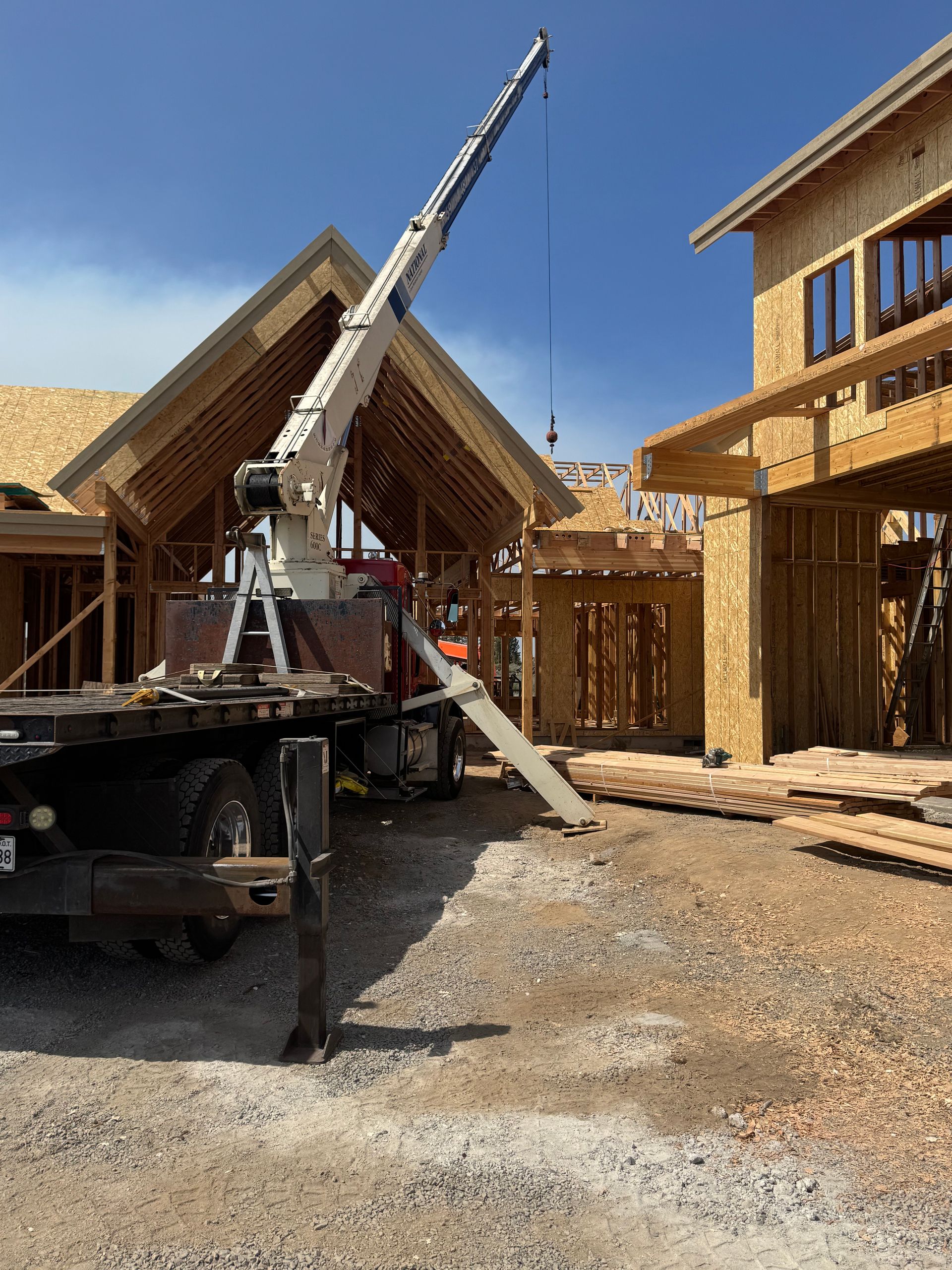 A truck with a crane on the back is parked in front of a house under construction.