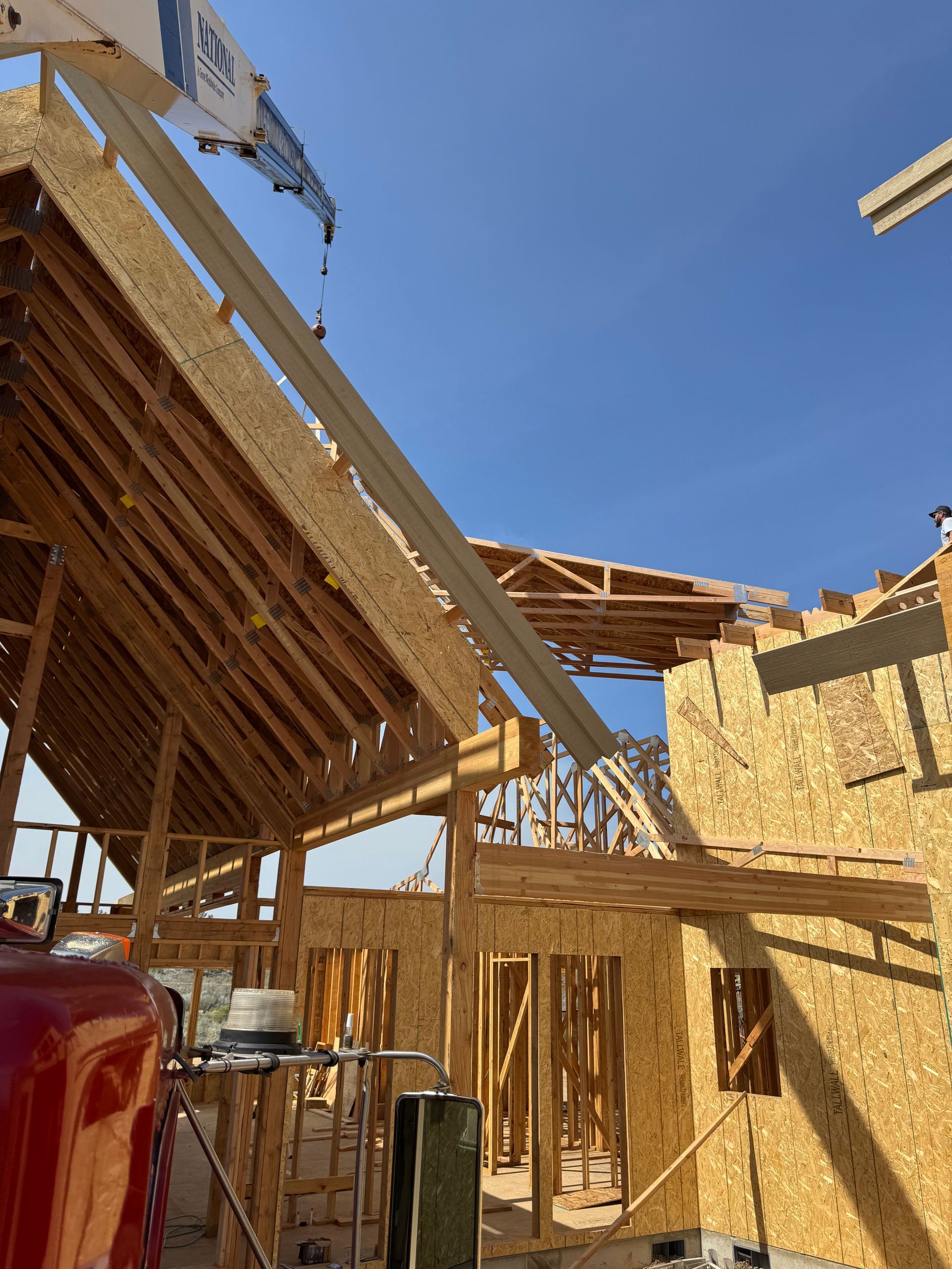 A crane is lifting a piece of wood on top of a building under construction