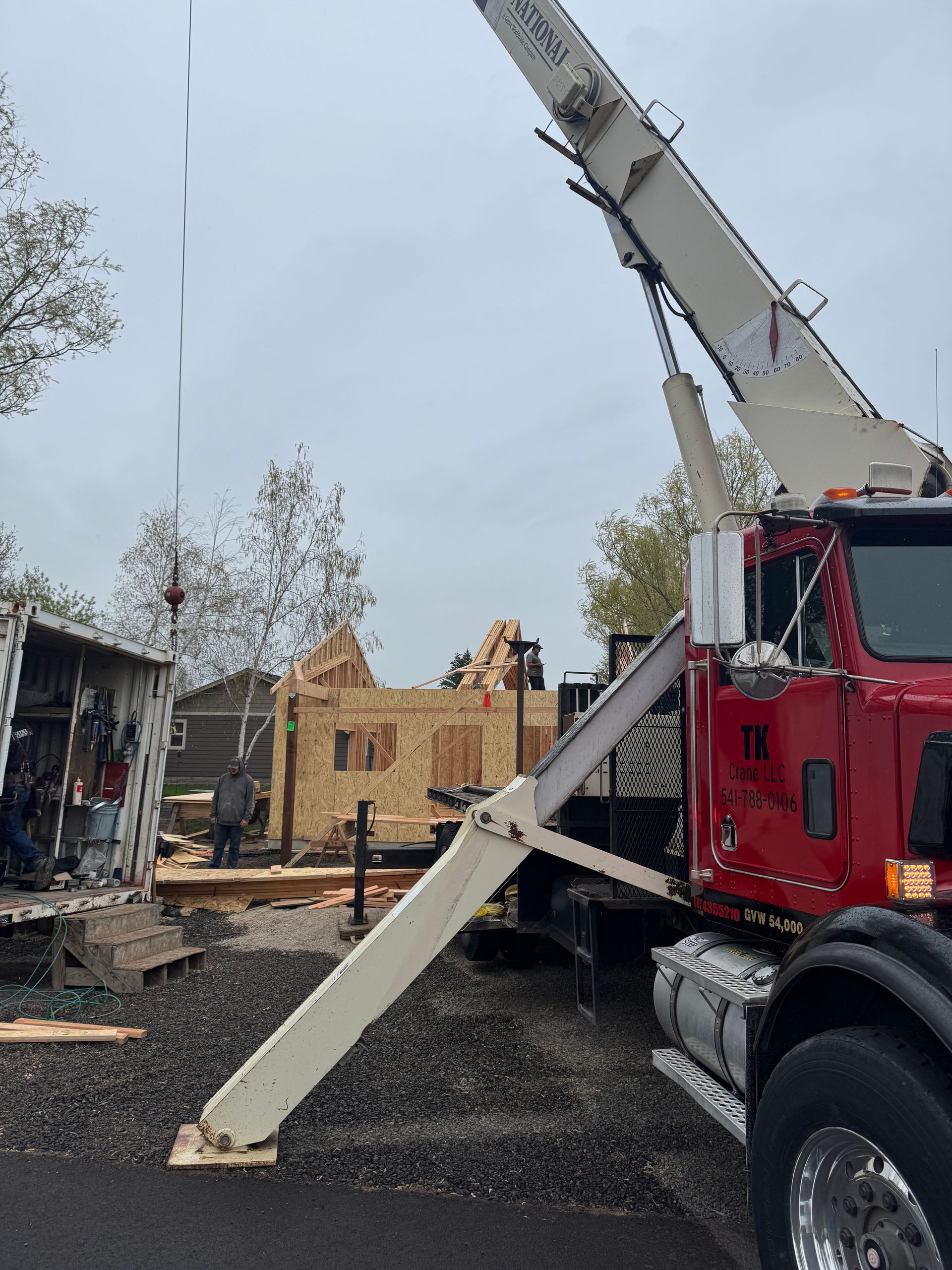A red truck with a crane attached to it is parked in front of a building under construction.