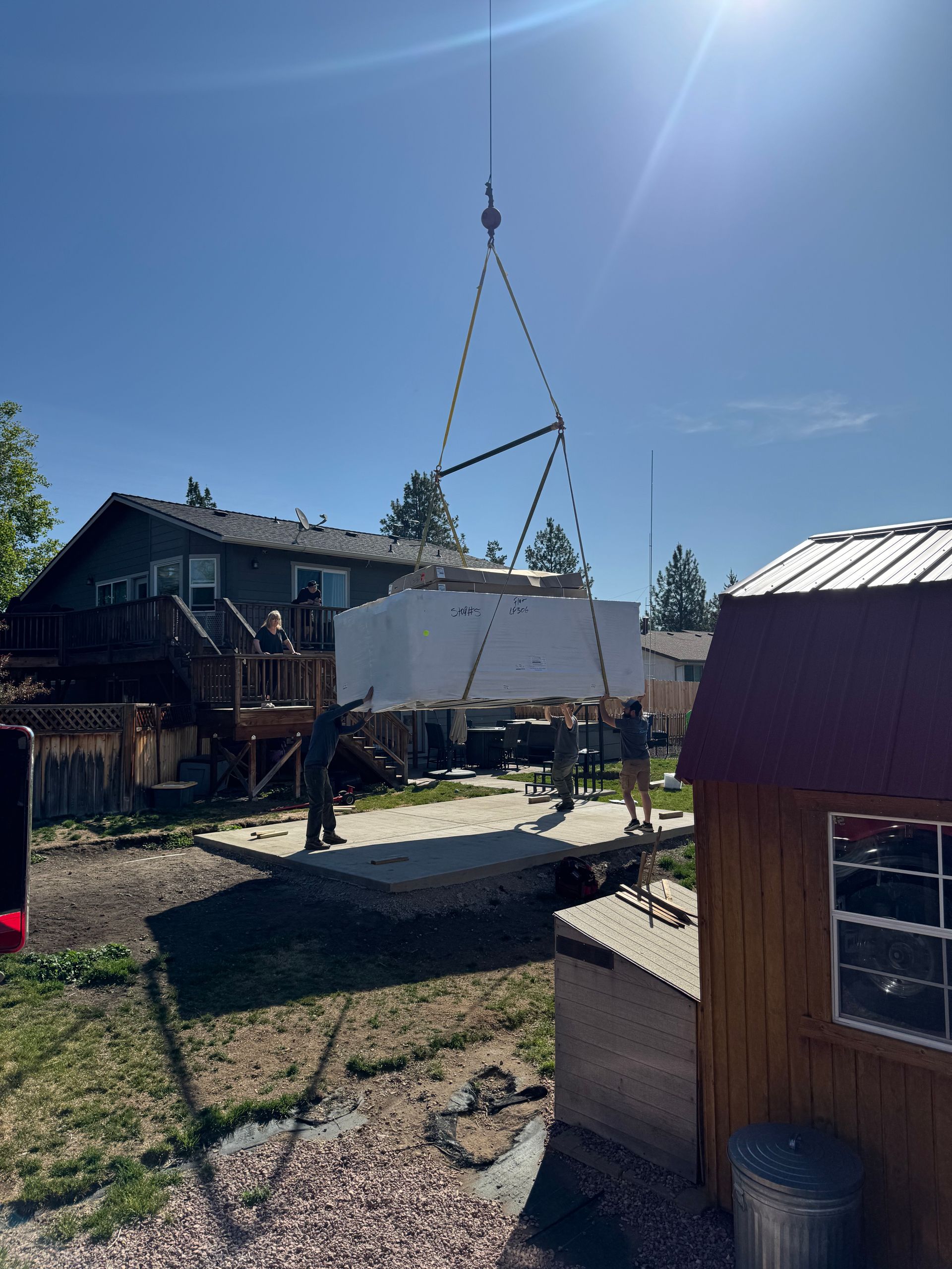 A large white box is being lifted by a crane in a backyard.