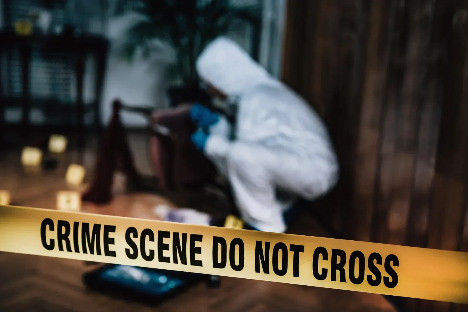 Crime scene: Investigator in hazmat suit, examining evidence behind caution tape.