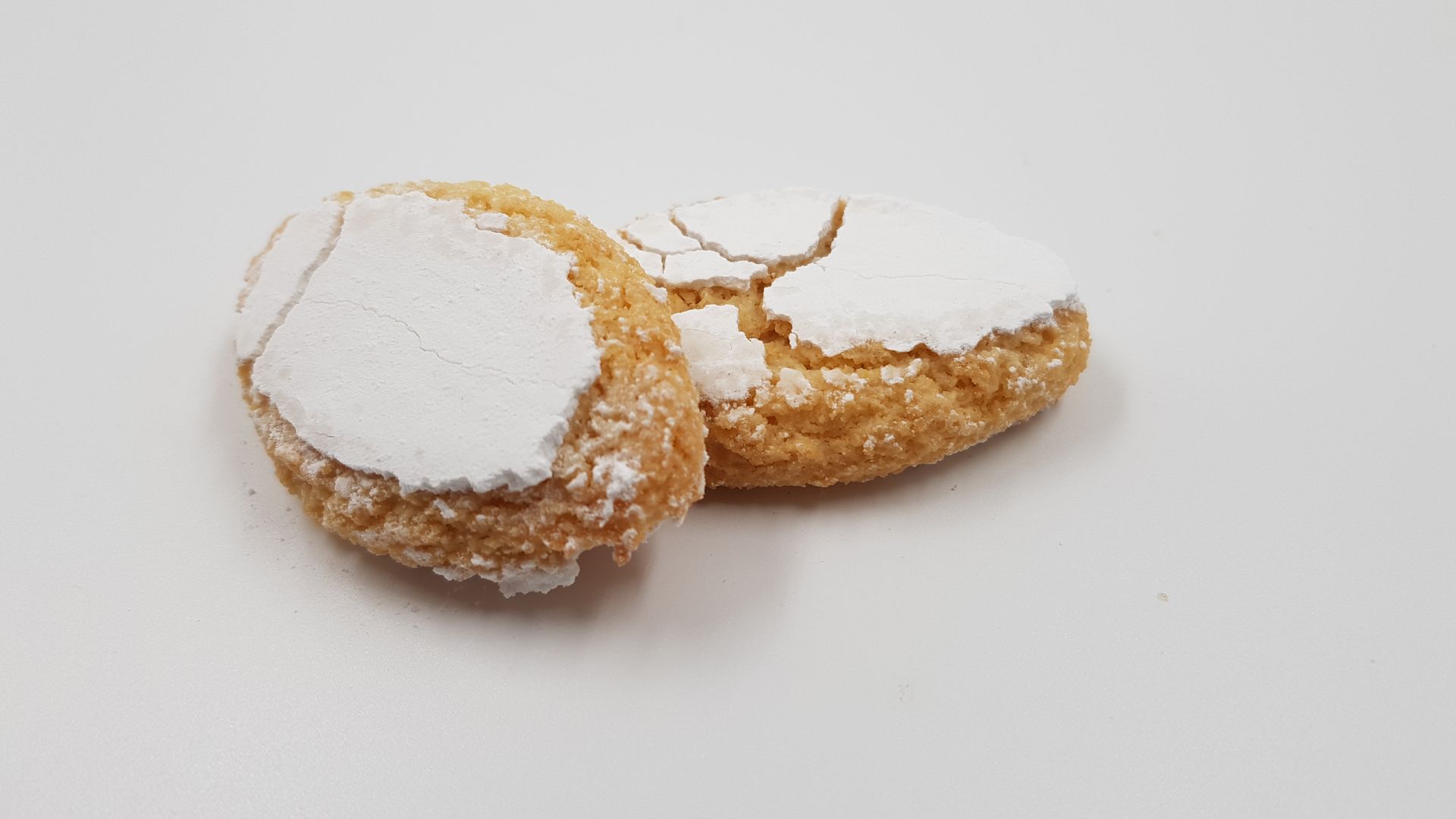 Due biscotti spolverati di zucchero a velo su una superficie bianca.