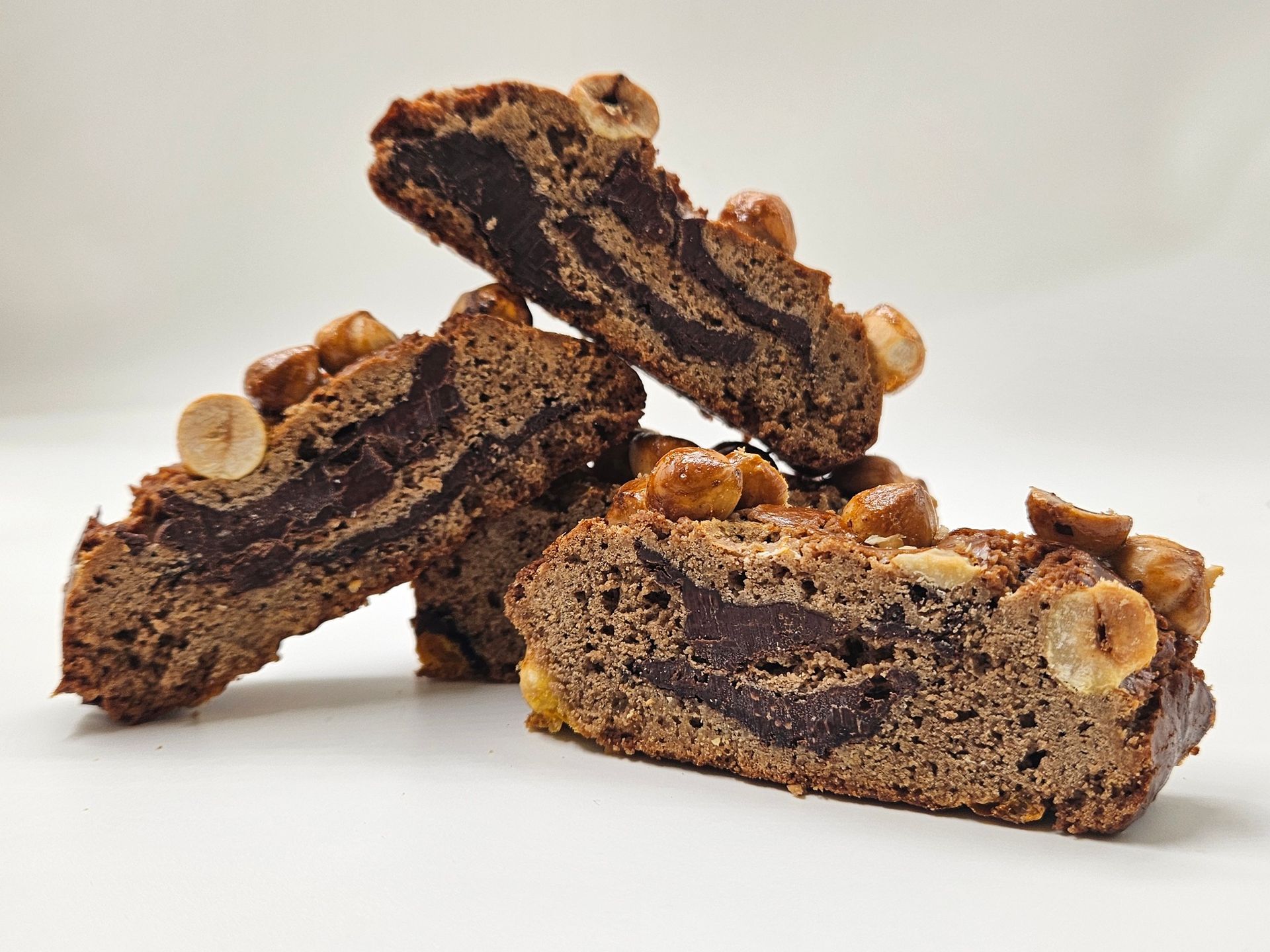 Tre fette di torta al cioccolato con sopra delle noci sono disposte una sopra l'altra su una superficie bianca.