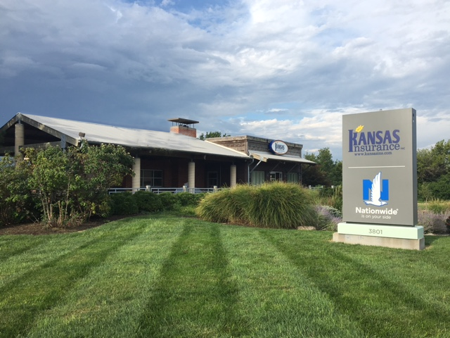 a large building with a kansas insurance sign in front of it and a lush green lawn .