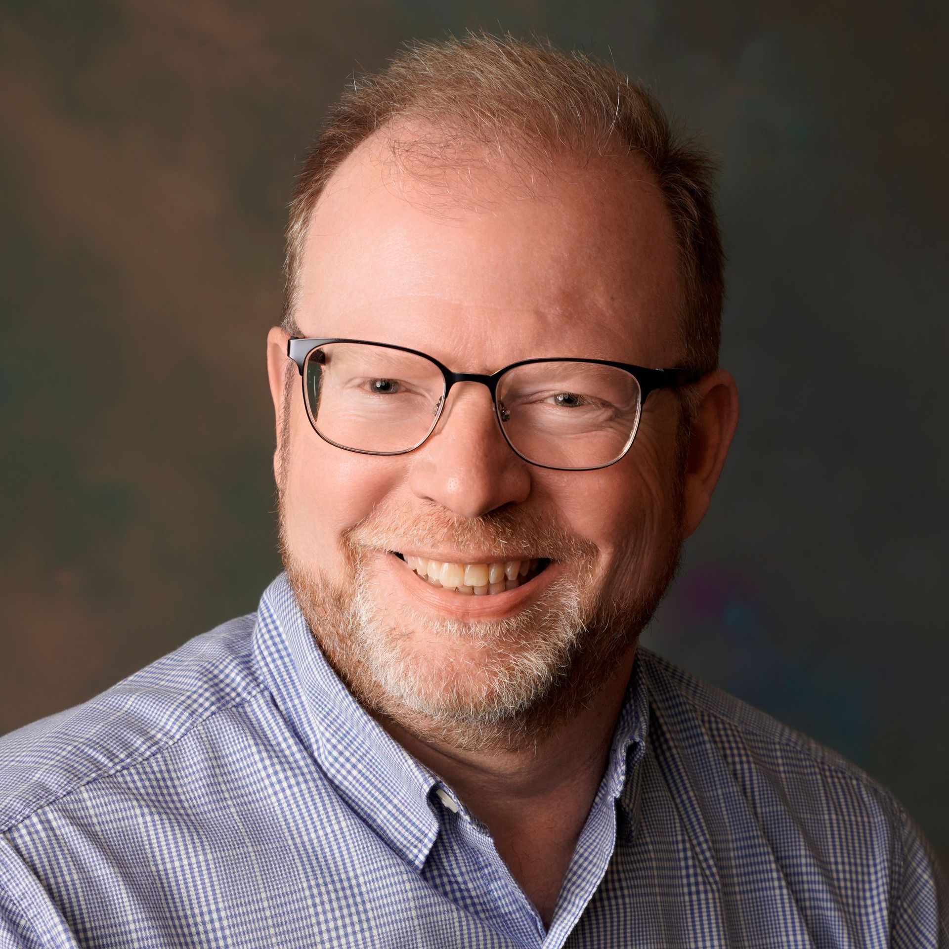 A man with glasses and a beard is smiling for the camera.