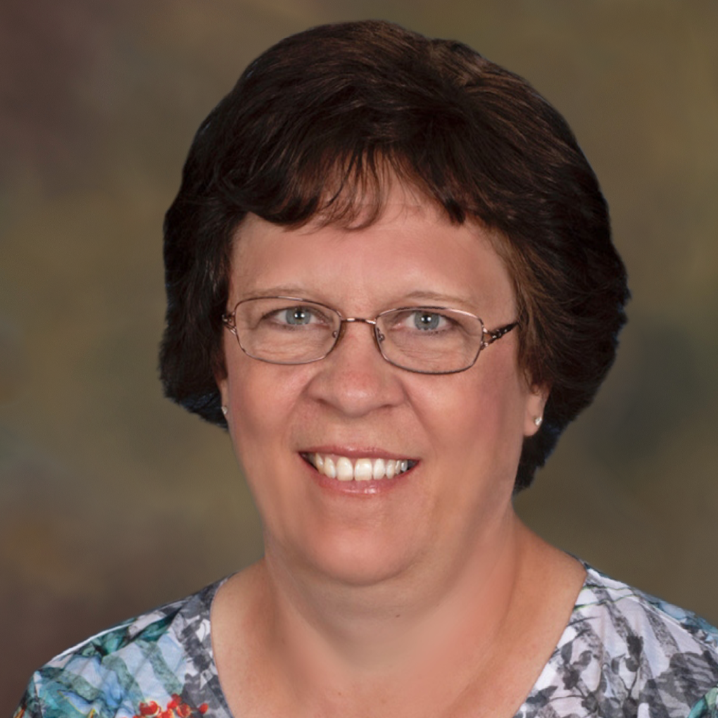 A woman wearing glasses and a floral shirt is smiling for the camera.