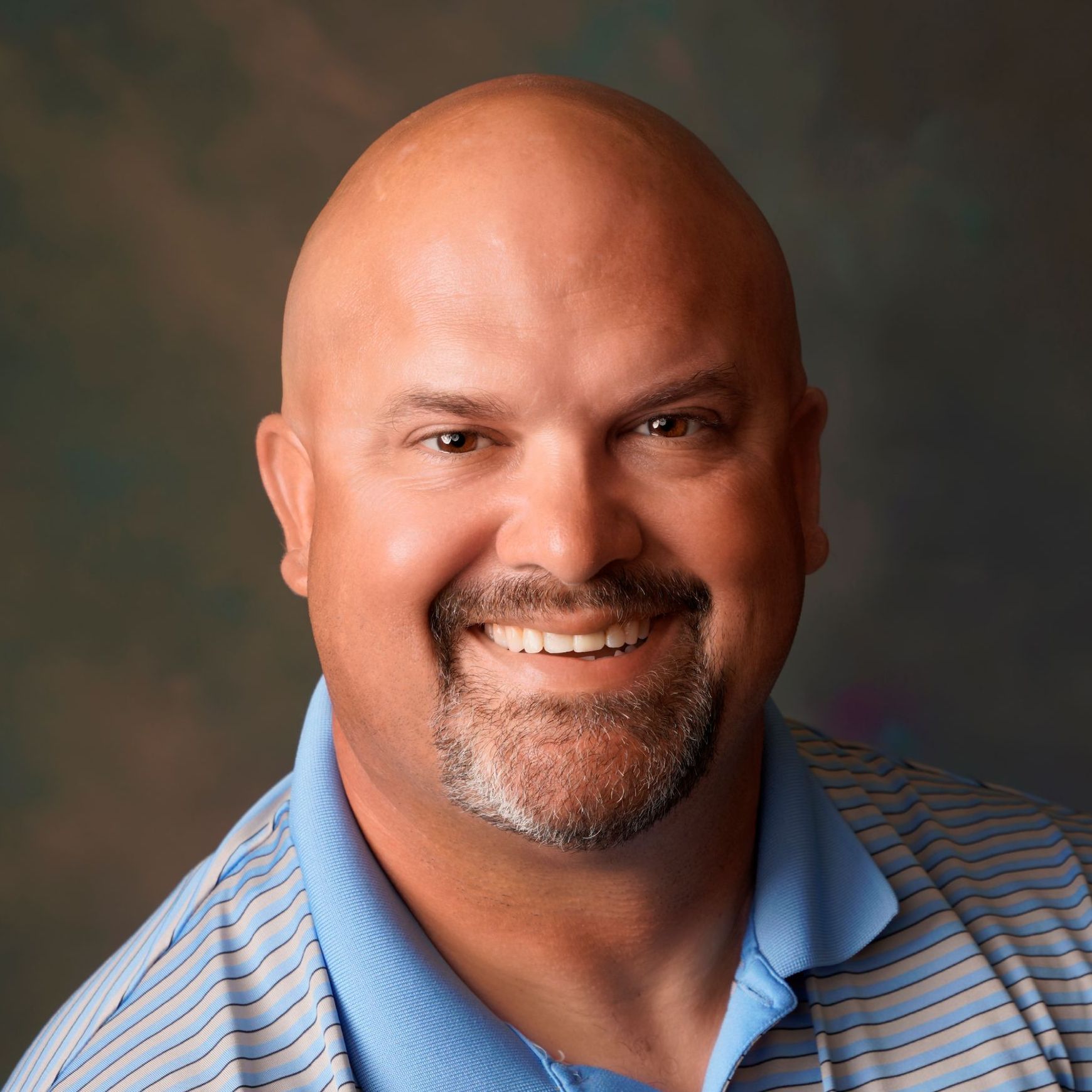 A bald man with a beard is smiling for the camera