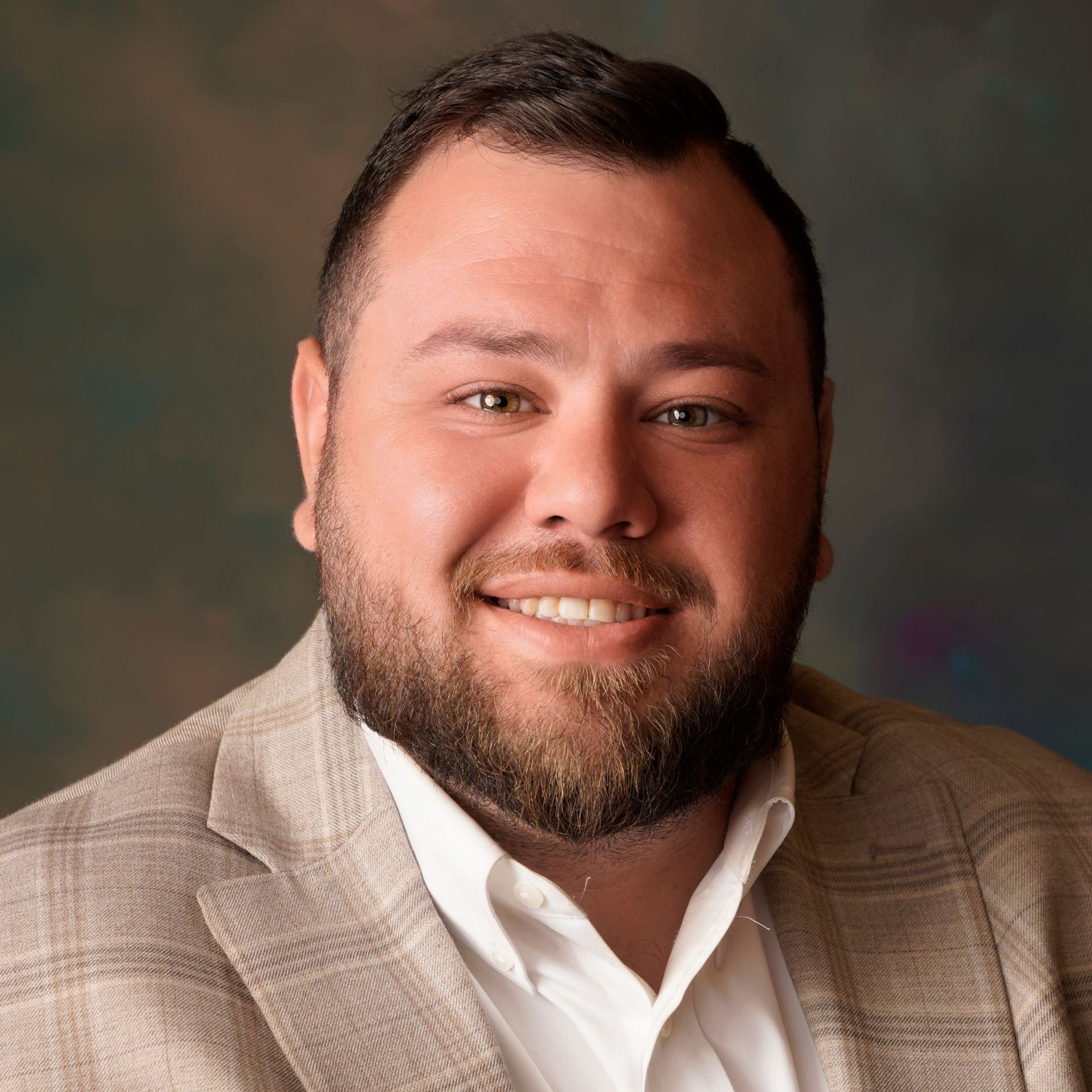 A man with a beard is wearing a suit and smiling for the camera