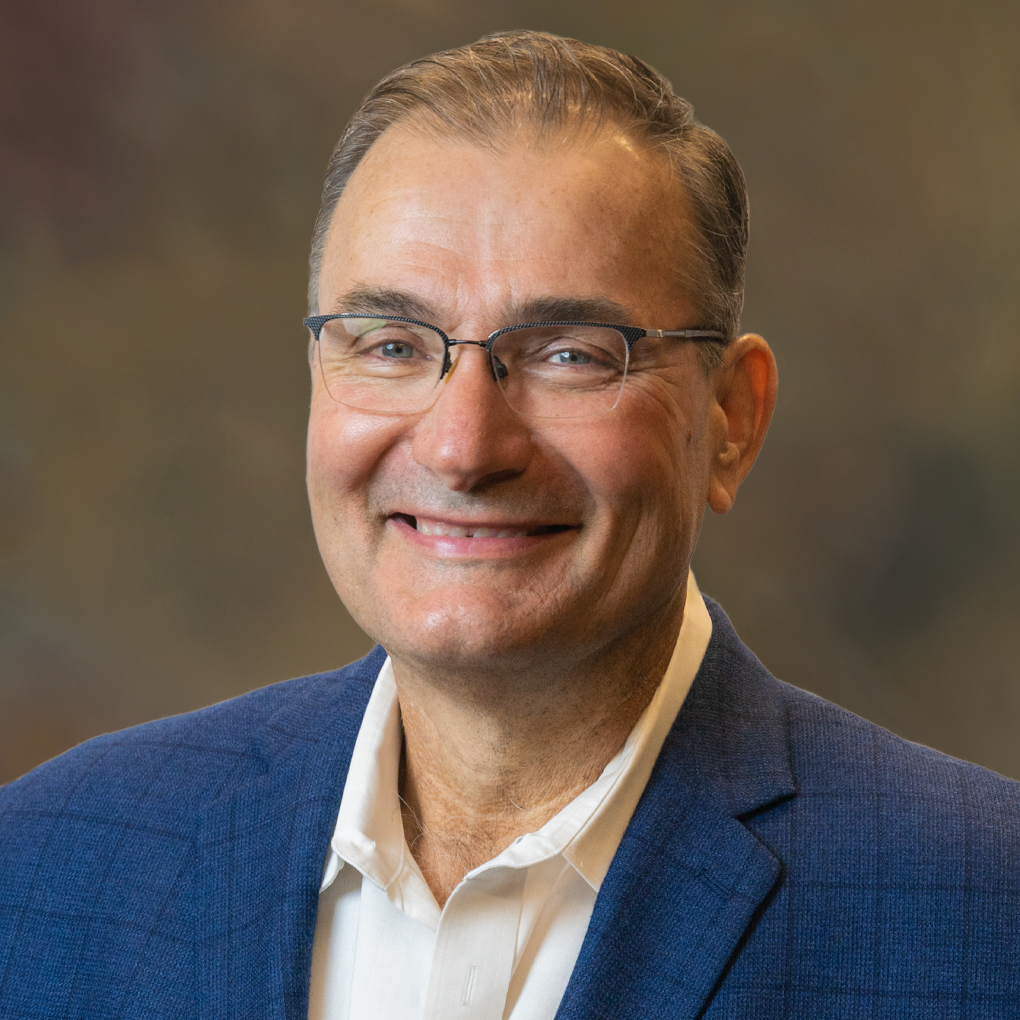 A man wearing glasses and a blue suit is smiling for the camera.