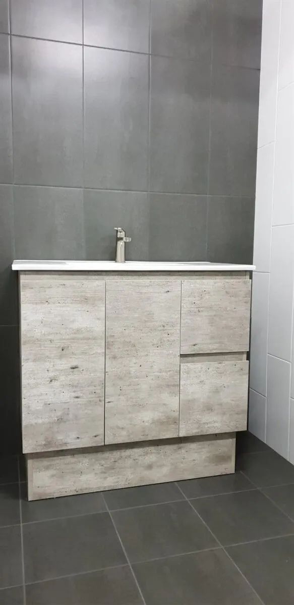 A Bathroom Vanity With a Light Wood-look Cabinet, White Countertop, and Silver Faucet Against Gray Tiled Walls and Floor — North Coast Tiles in Maclean, NSW