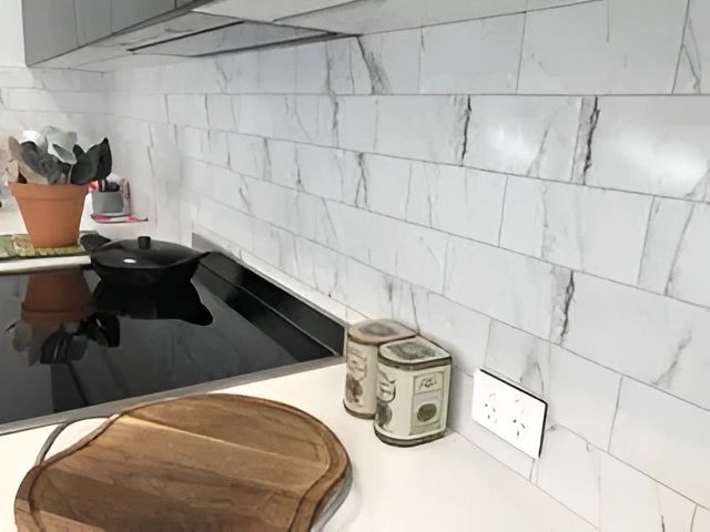 White Marble-effect Kitchen Backsplash With Black Stove Top and Wooden Cutting Board in a Modern Kitchen Setting — North Coast Tiles in Maclean, NSW