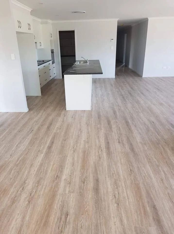Interior View of a Modern Home With Light Wood-look Flooring, White Walls, and a Kitchen With a Dark Countertop — North Coast Tiles in Maclean, NSW