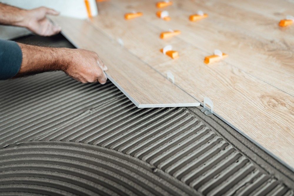 A Person Laying Wood-look Floor Tiles on a Textured Gray Adhesive — North Coast Tiles in Grafton, NSW