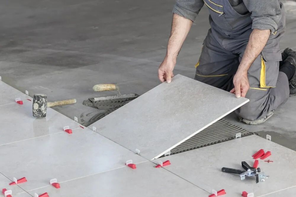 A Person Installing Floor Tiles in a Room; He's Holding a Tile Above the Adhesive-covered Underlayment — North Coast Tiles in Grafton, NSW