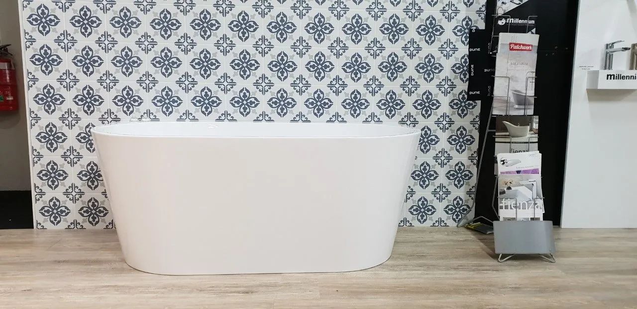 A Freestanding White Bathtub is Displayed in Front of a Patterned Blue and White Wall. a Brochure Stand is to the Right of the Tub — North Coast Tiles in Iluka, NSW