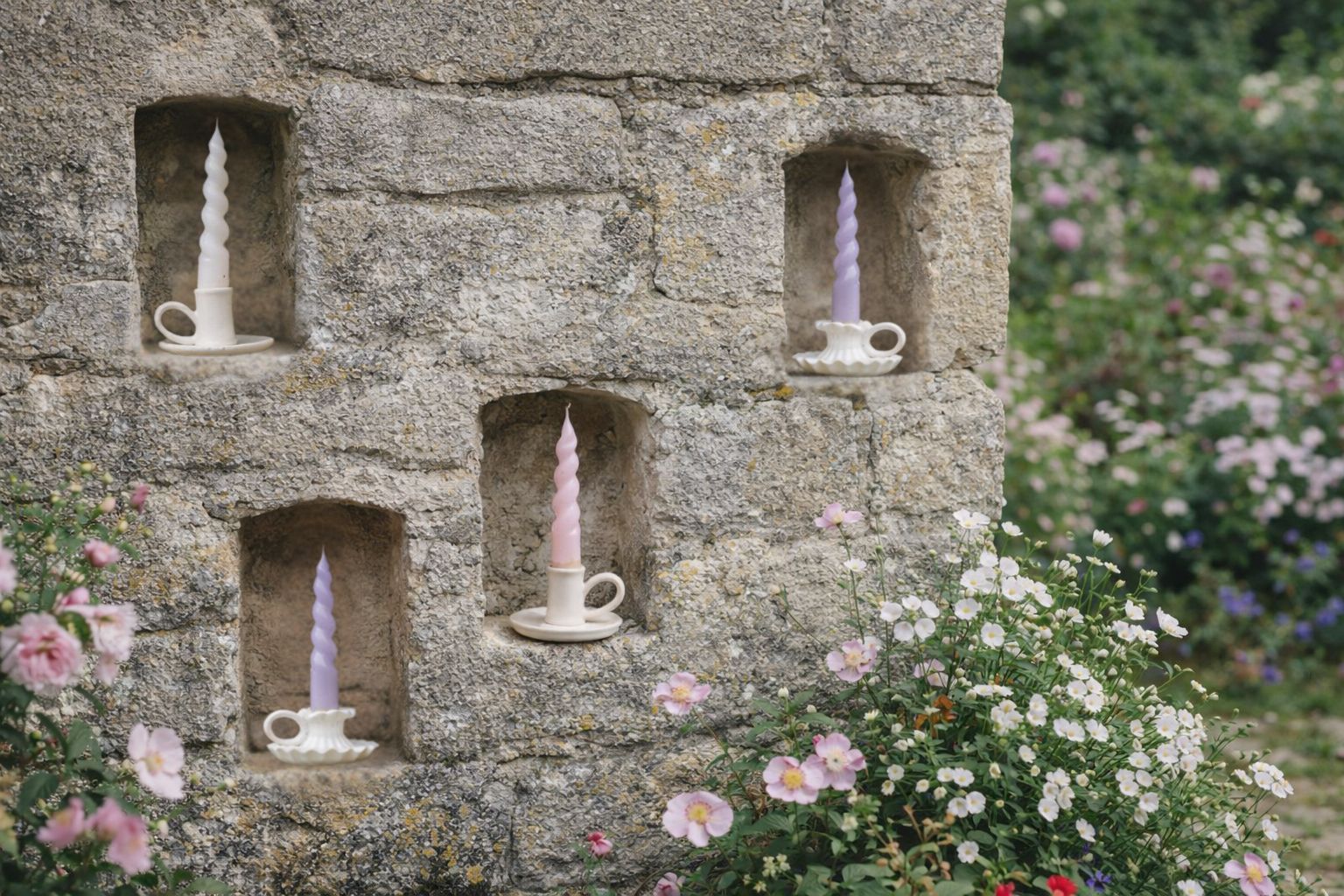 Cream ceramic handmade vintage style candle holders in a stone garden wall setting surrounded by cottage garden flowers