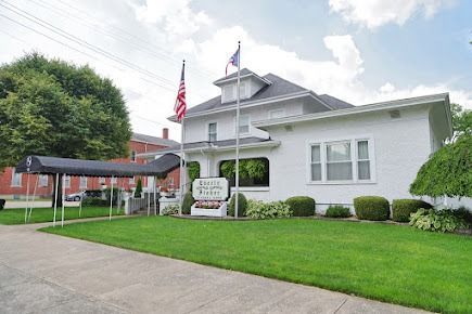 White building with awning, green lawn, American flags. Sign says 