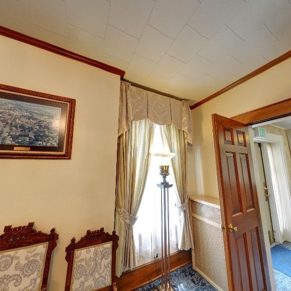 A room with a framed picture, chairs, window with curtains, and a door.