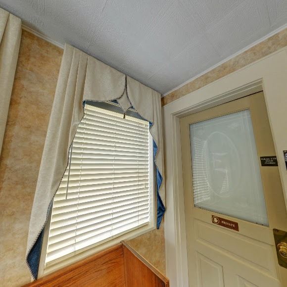 Window with blinds and curtain next to a door in a room with light-colored walls and wood trim.